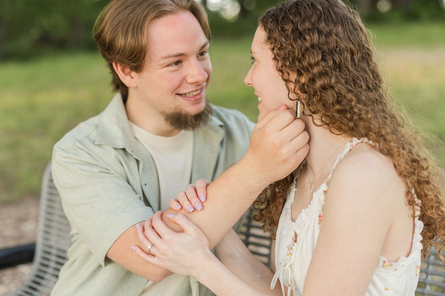A couple shares an intimate moment outdoors, with her long curly hair and his grey shirt against a natural background.