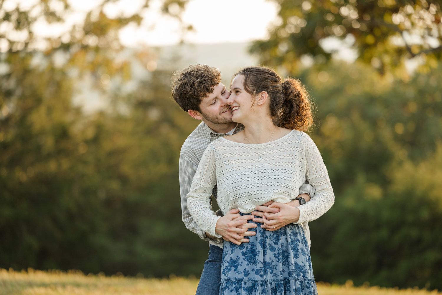 A couple shares a romantic embrace in a sunlit field during golden hour.