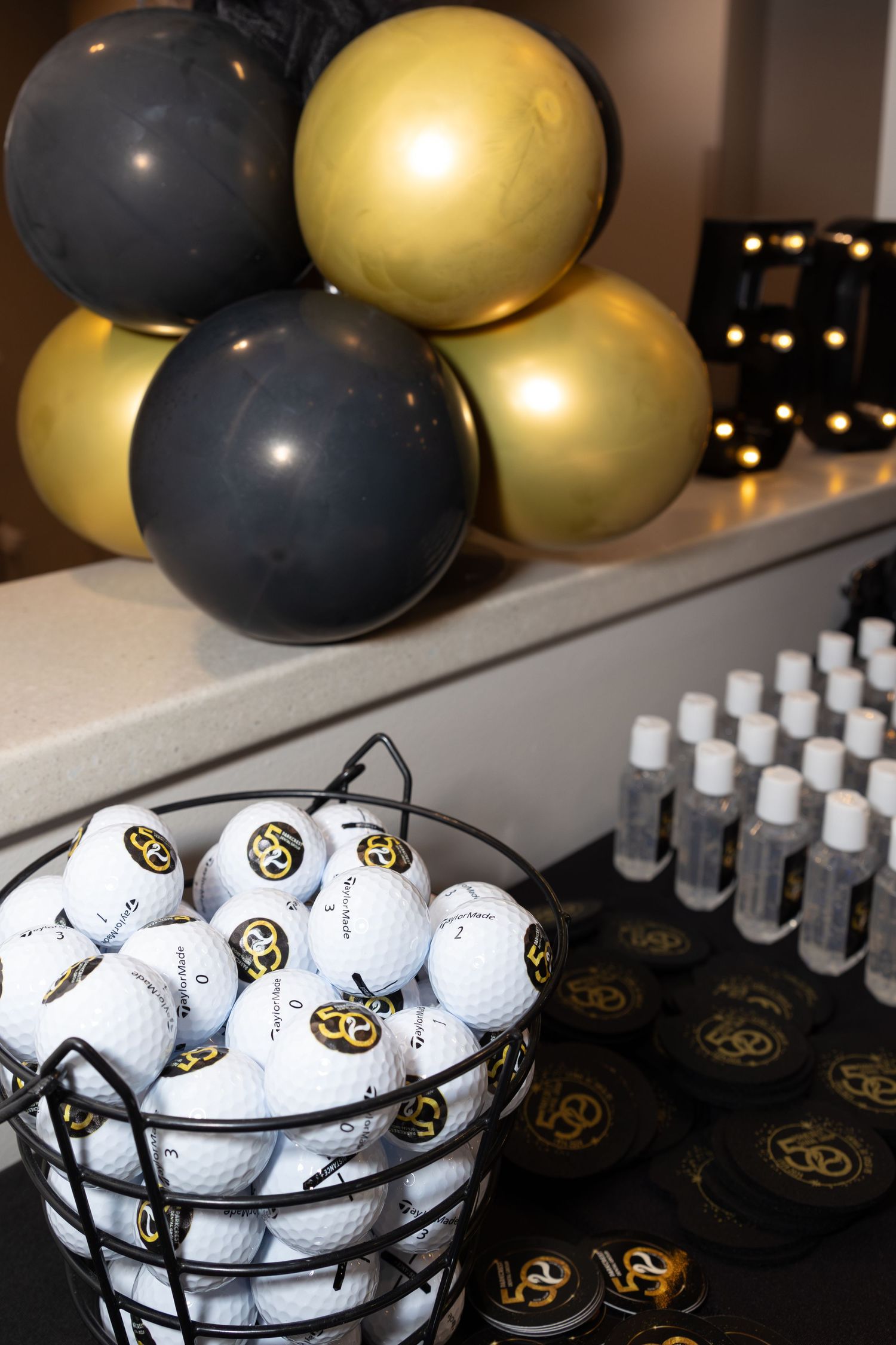 Golf balls and promotional items displayed with black and gold balloons at an event.