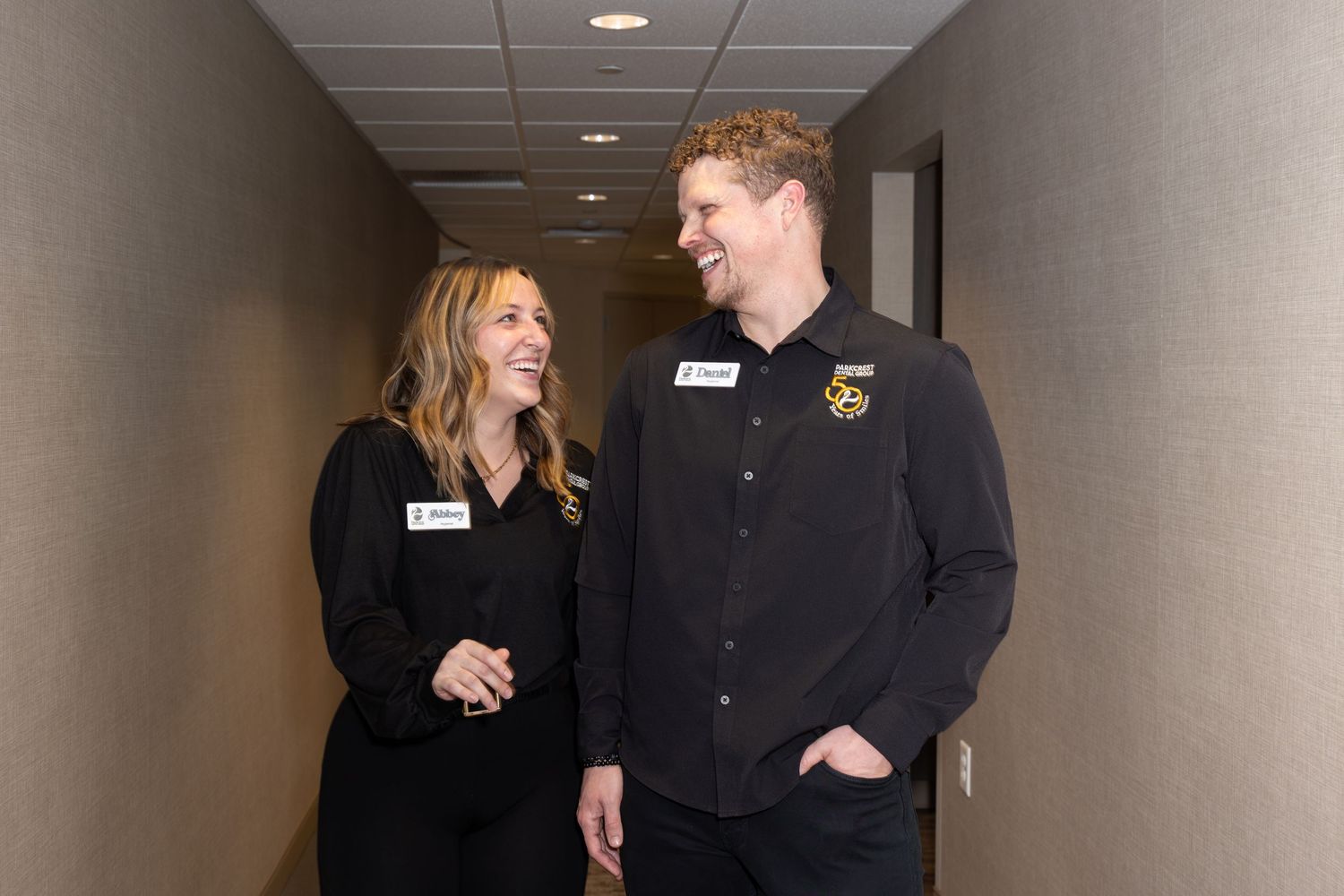 Two colleagues engaging in conversation while standing in an office hallway.