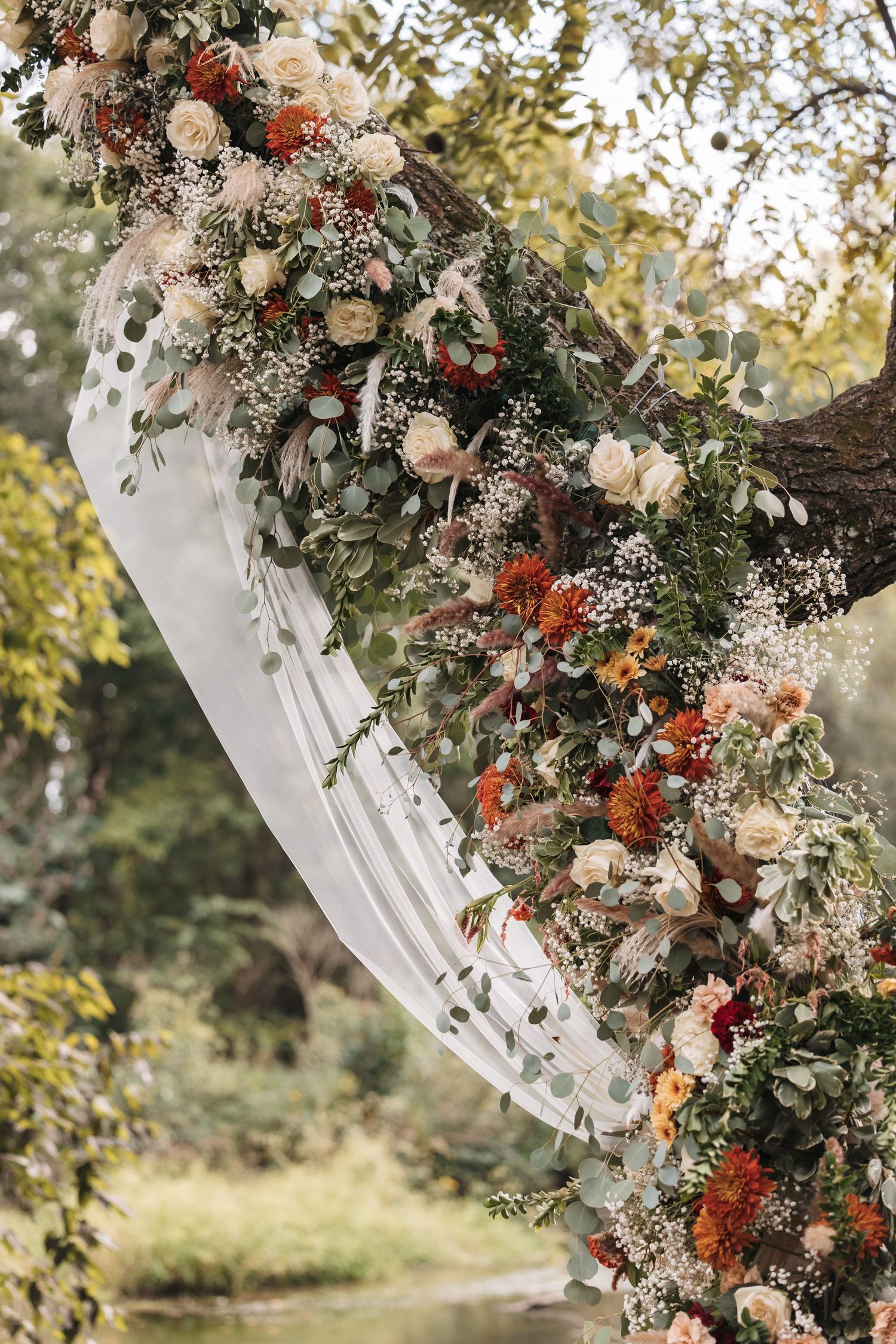 Elegant floral arch with white and coral flowers adorned with greenery for wedding ceremony.