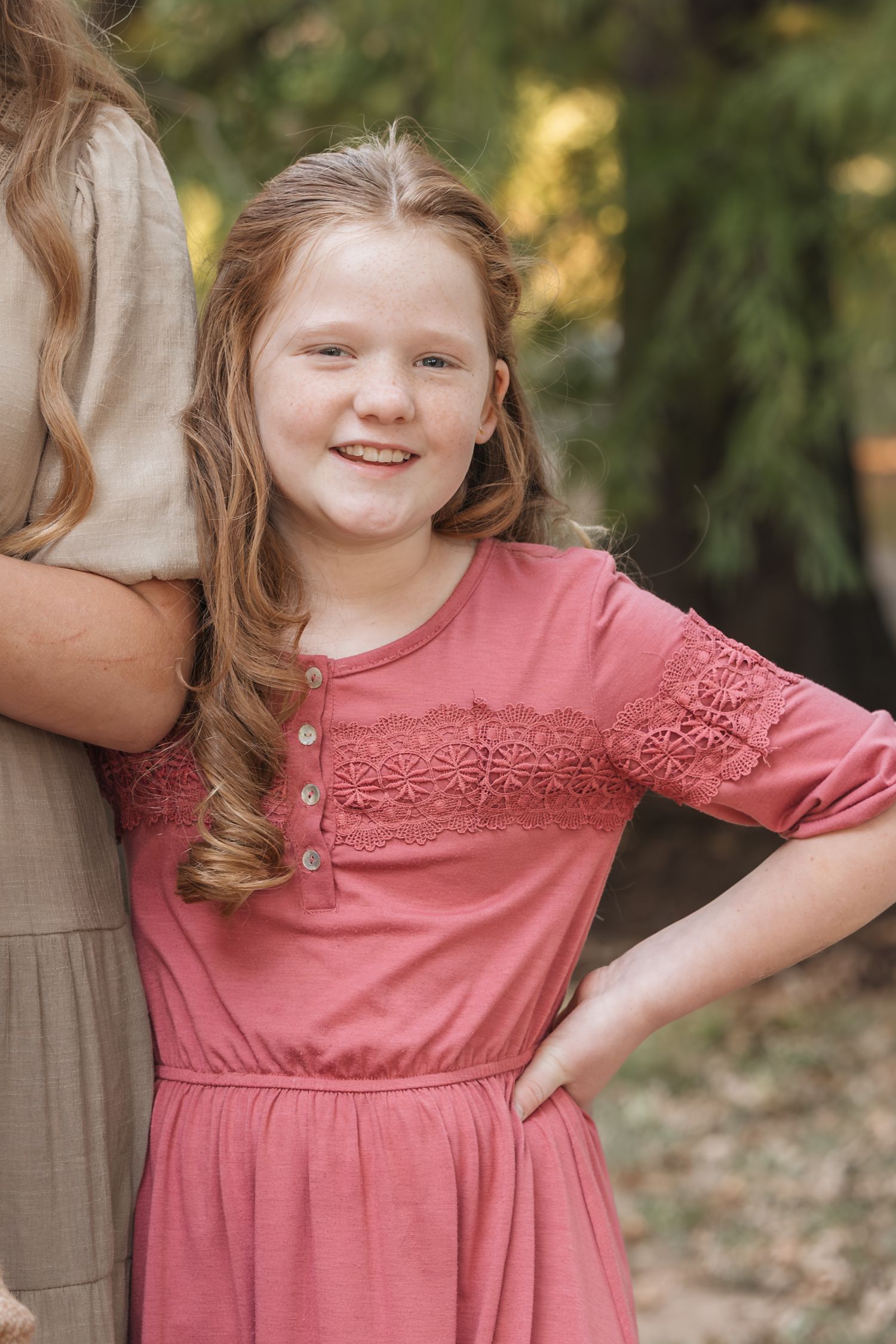 Portrait in coral pink dress with lace details against natural backdrop.