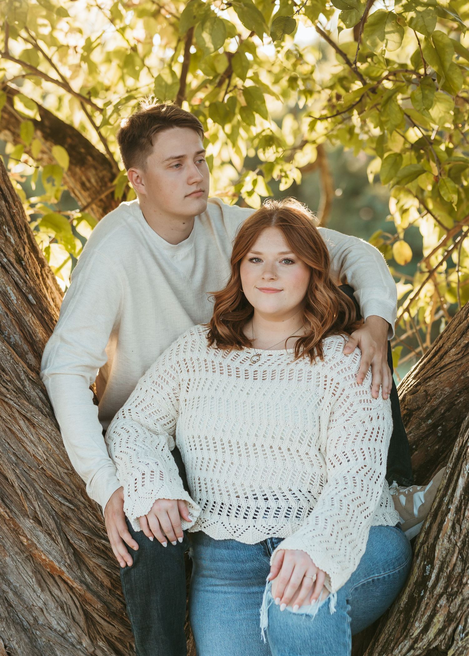 Two people share an intimate moment while sitting in a large forked tree trunk.