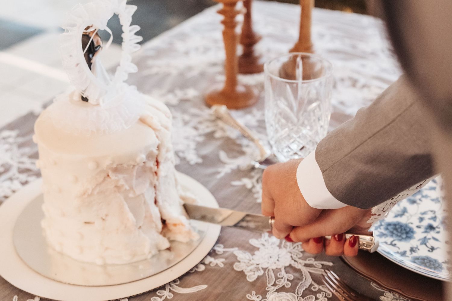 White wedding cake with elegant lace details and crystal glassware on a decorated table.