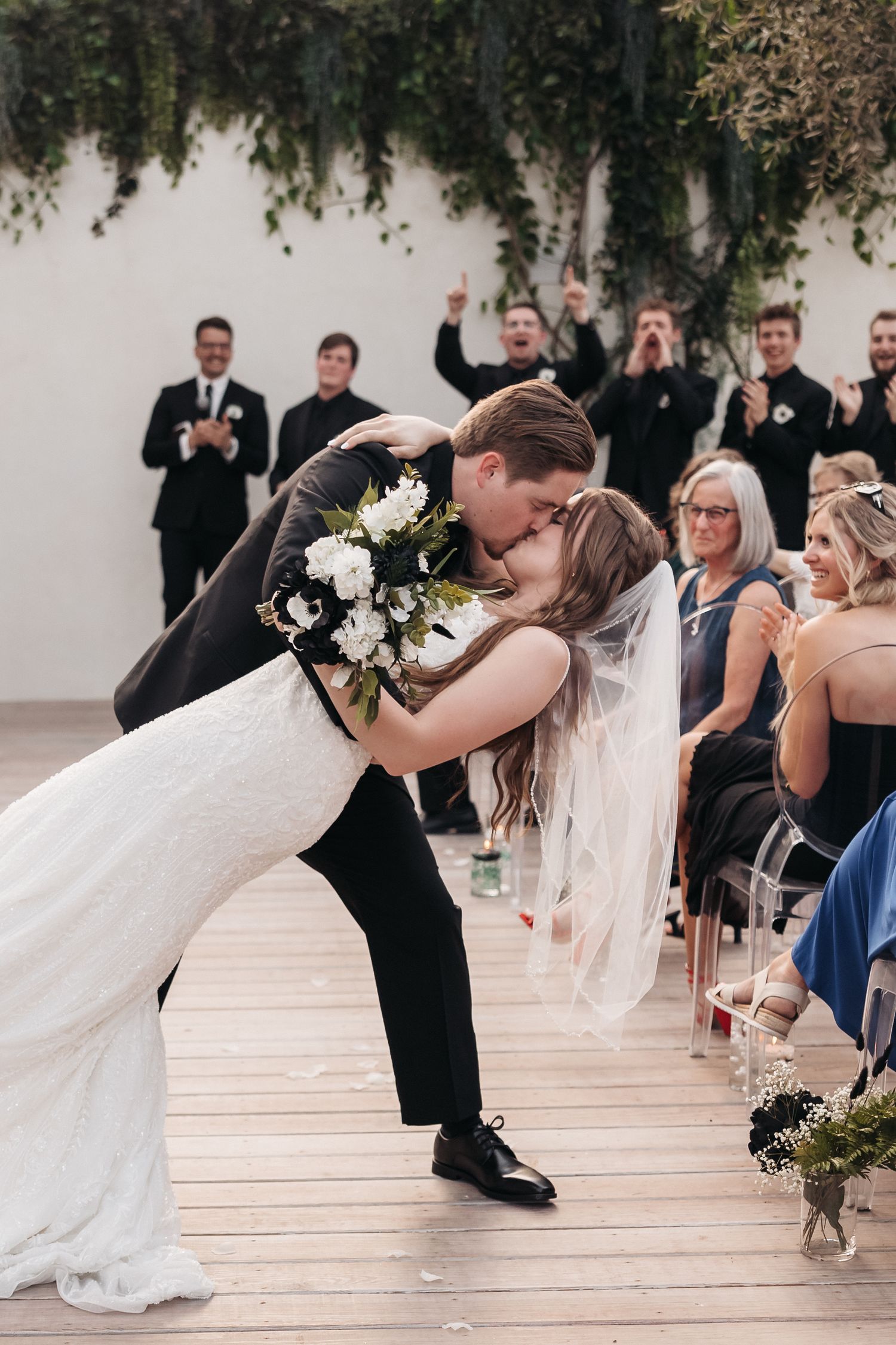 A romantic dip kiss during a wedding ceremony with guests applauding in the background.