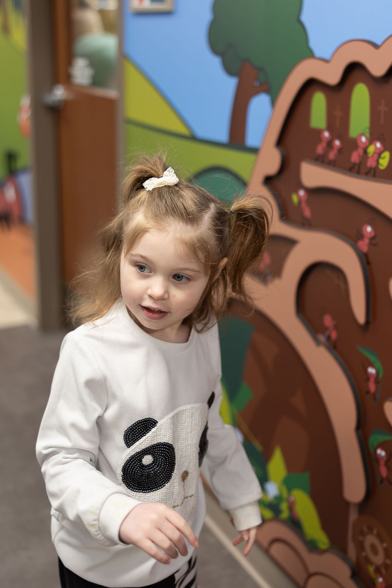 A child in a panda sweater exploring interactive wall art in a decorated hallway.