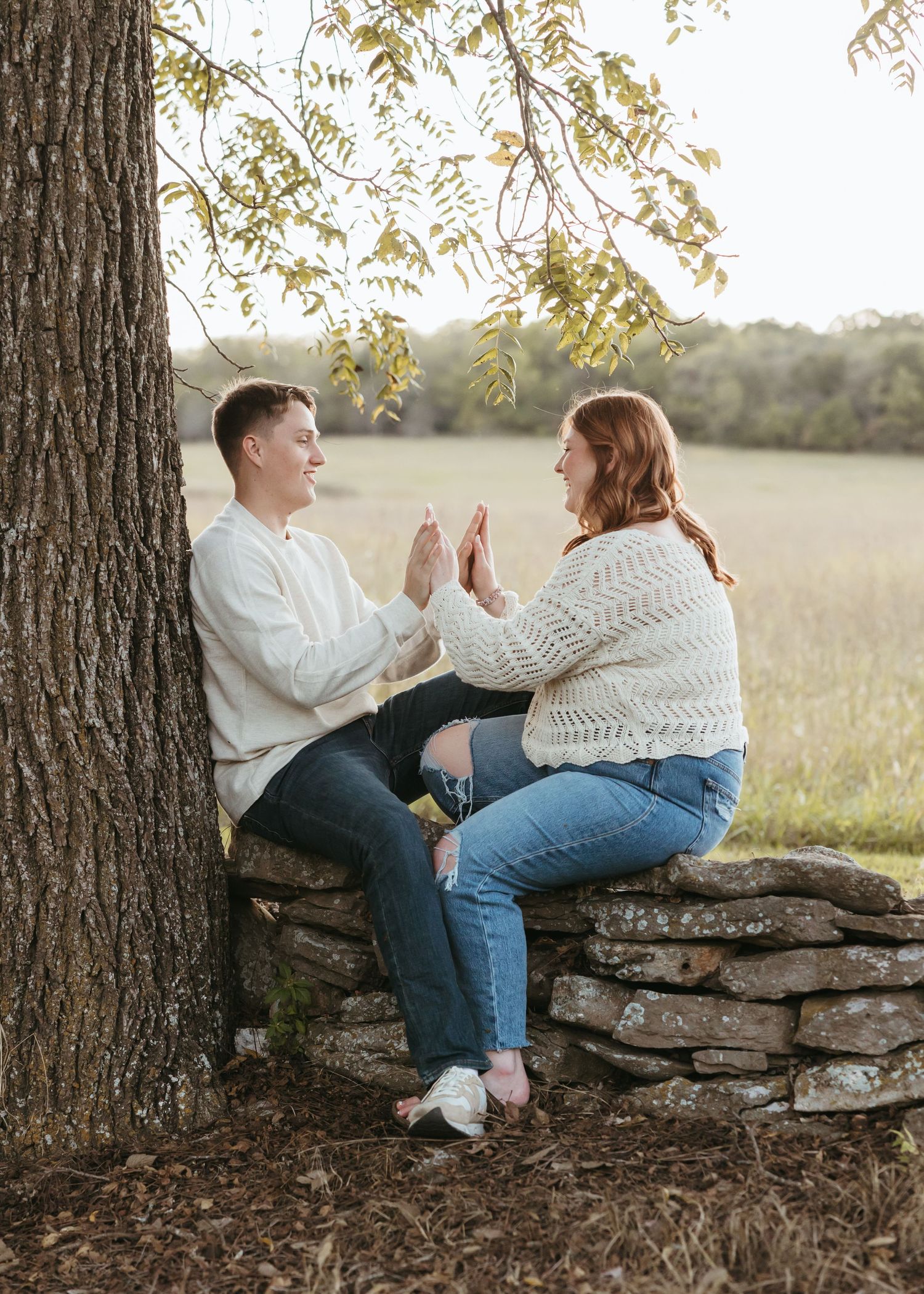 Two people play a hand clapping game while sitting on a stone wall.