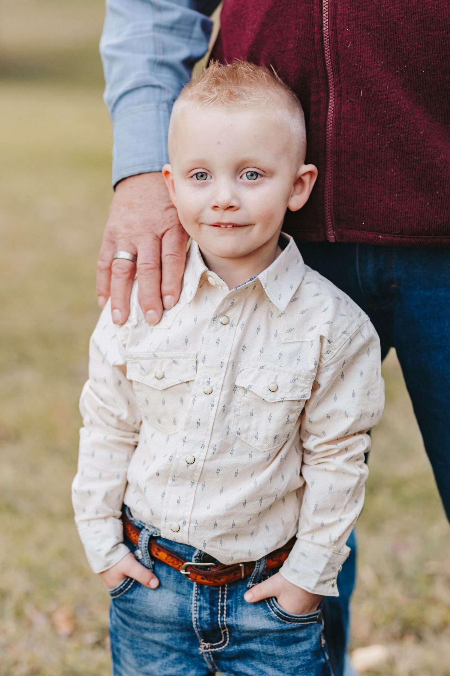 Child in light colored western shirt and jeans stands outdoors.