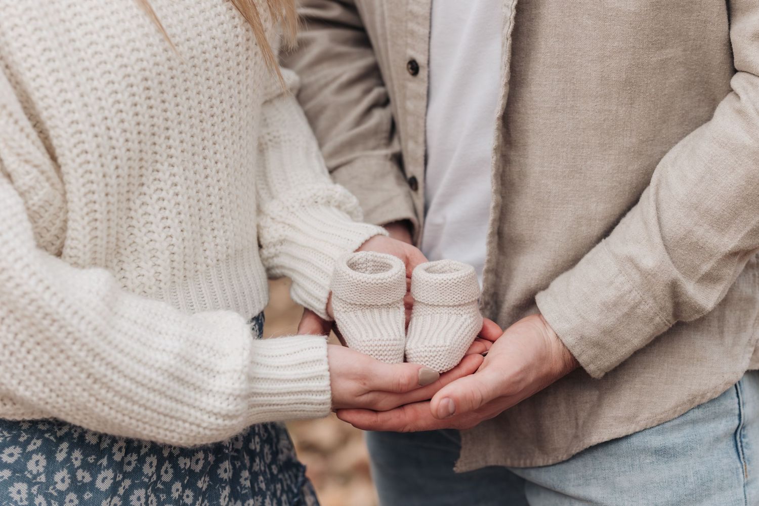 Close-up of hands holding tiny baby shoes in soft natural light.
