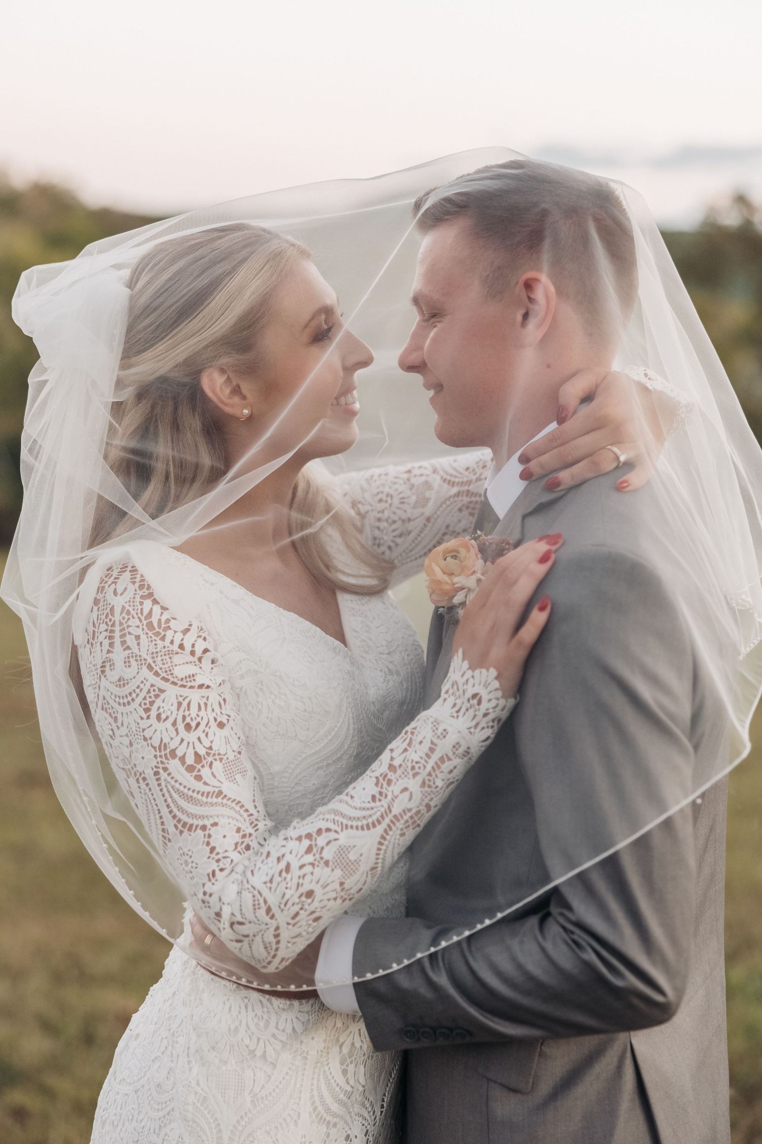 Romantic wedding moment with couple embracing under lace veil in outdoor setting.