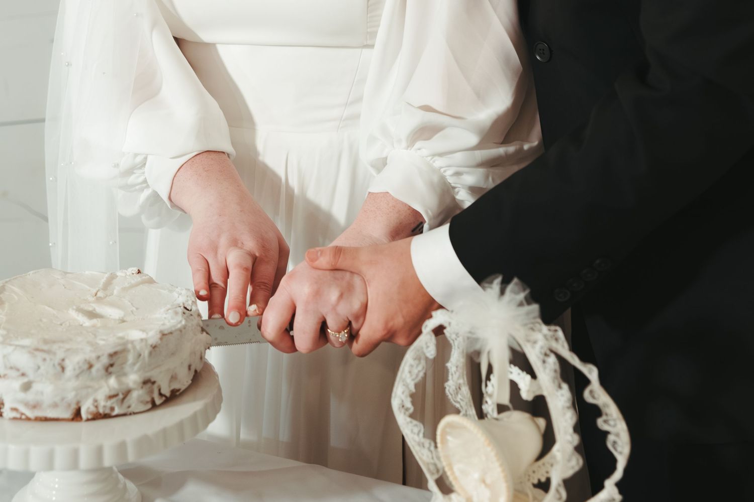 Close-up of hands cutting a white wedding cake with delicate decorations.