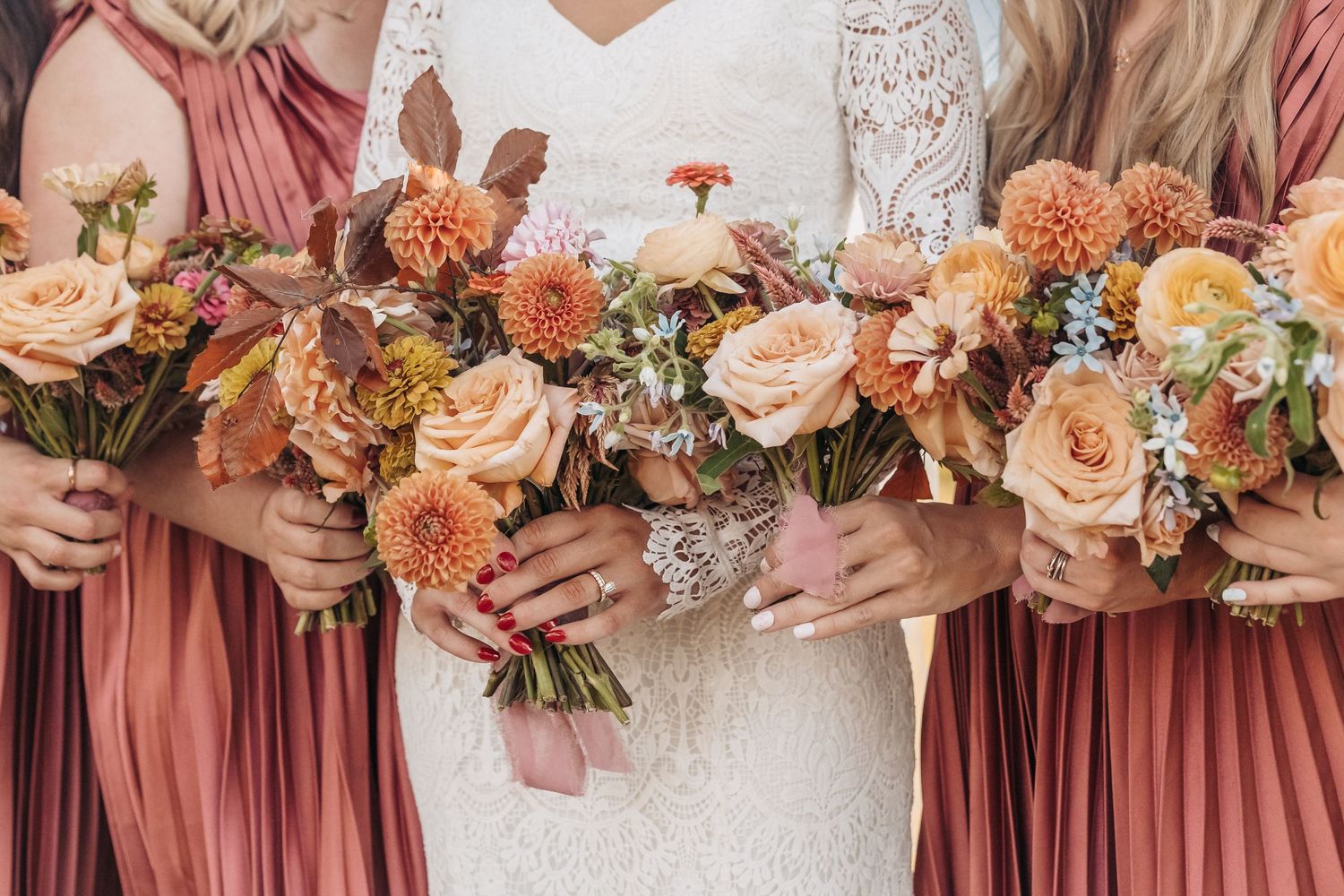 Close-up of wedding bouquets featuring peach dahlias, roses and fall foliage against mauve bridesmaid dresses.