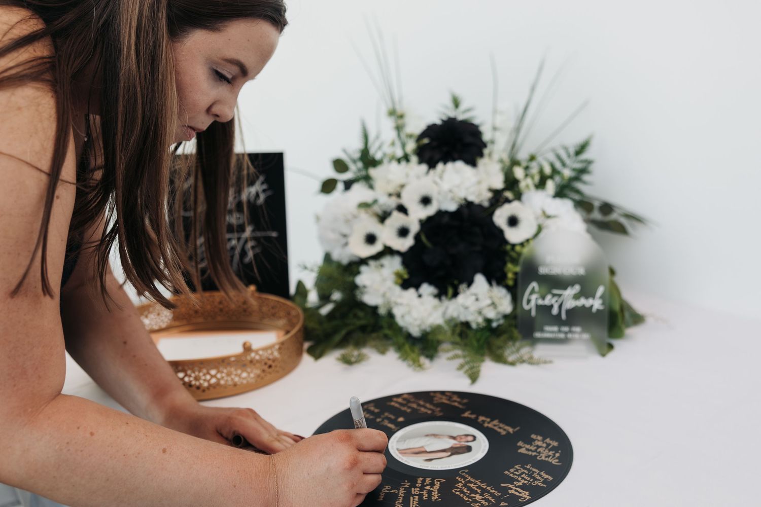 A person signs a black guest book with white flowers displayed in the background.