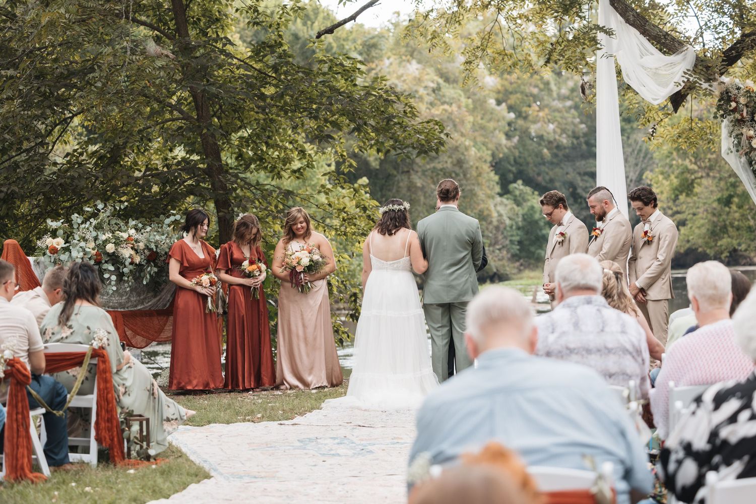 Outdoor wedding ceremony setup with rows of white chairs and guests in coral-colored dresses.