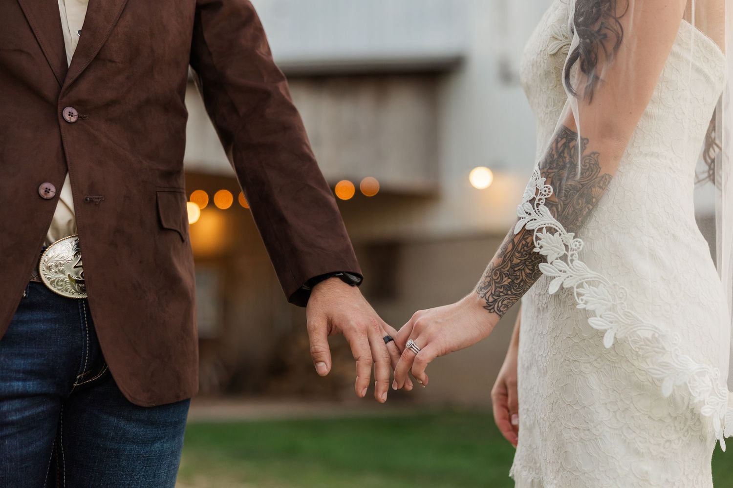 A couple holds hands while walking together, the bride in a white dress and groom in a brown suit jacket.