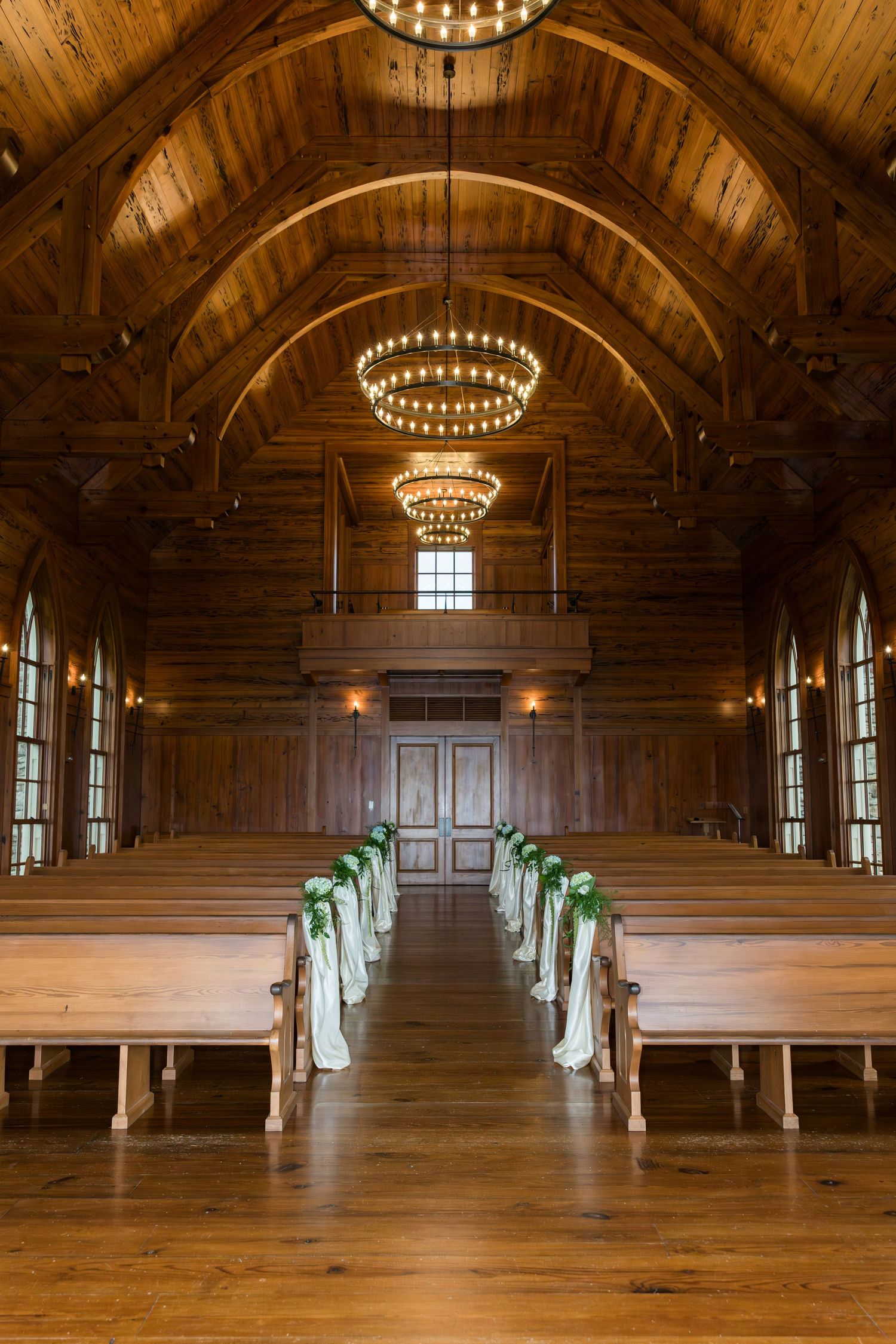 Rustic wooden chapel interior with vaulted ceiling, circular chandeliers and wooden pews decorated with mint green bows.