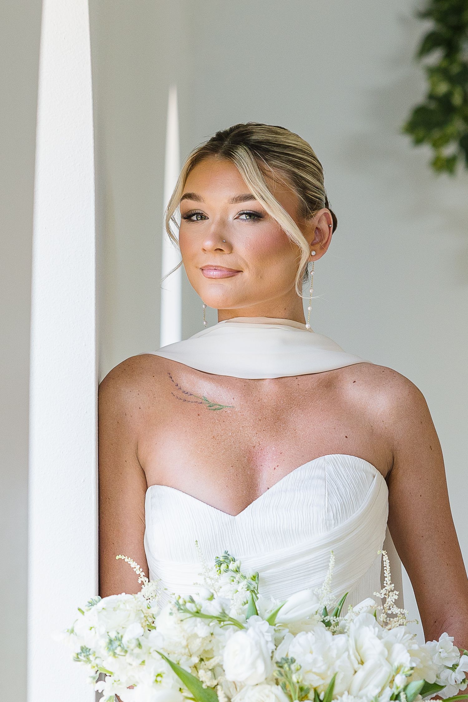 Beautiful bridal portrait showing a strapless white wedding gown and elegant white floral bouquet against a white column.