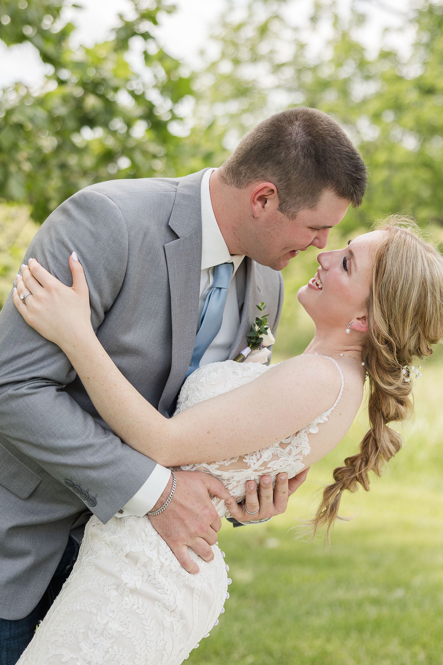 A romantic wedding photo shows a couple sharing an intimate dip pose outdoors with natural greenery in the background.