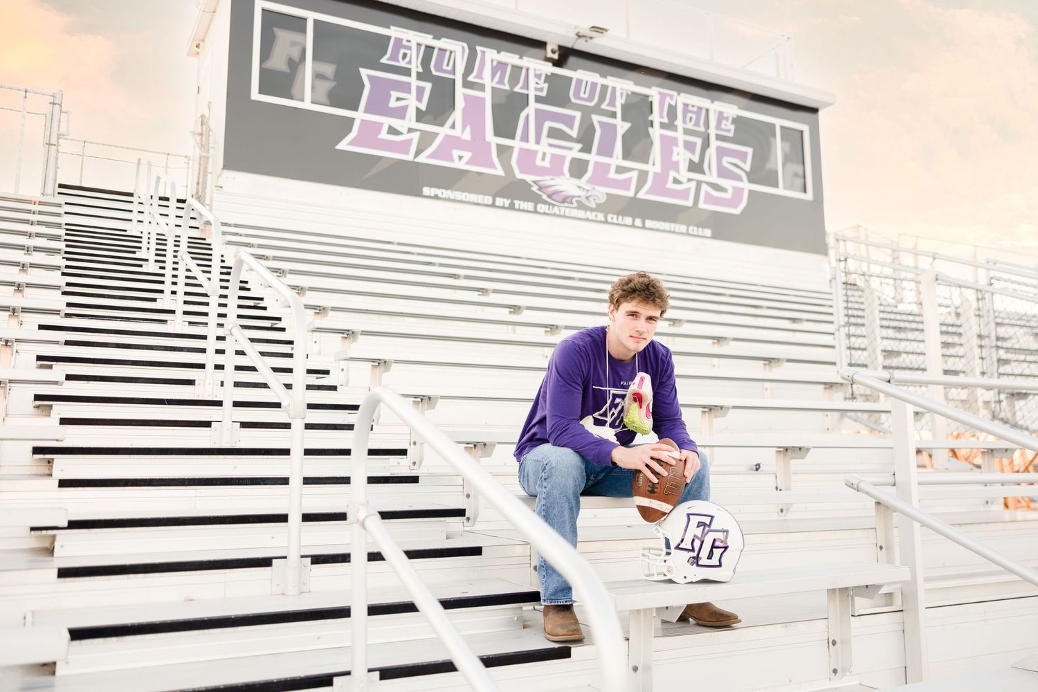Person sitting on bleachers at athletic field with purple lettering visible in background.