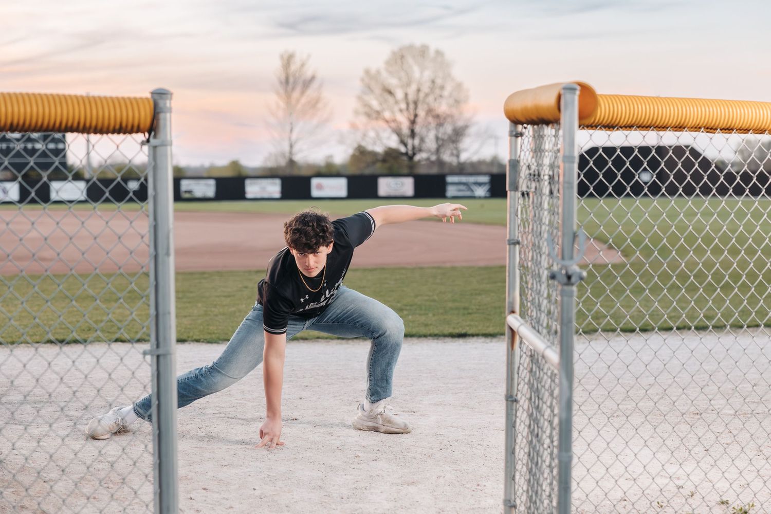 Athletic figure demonstrating fielding stance at baseball field with chain link fence.
