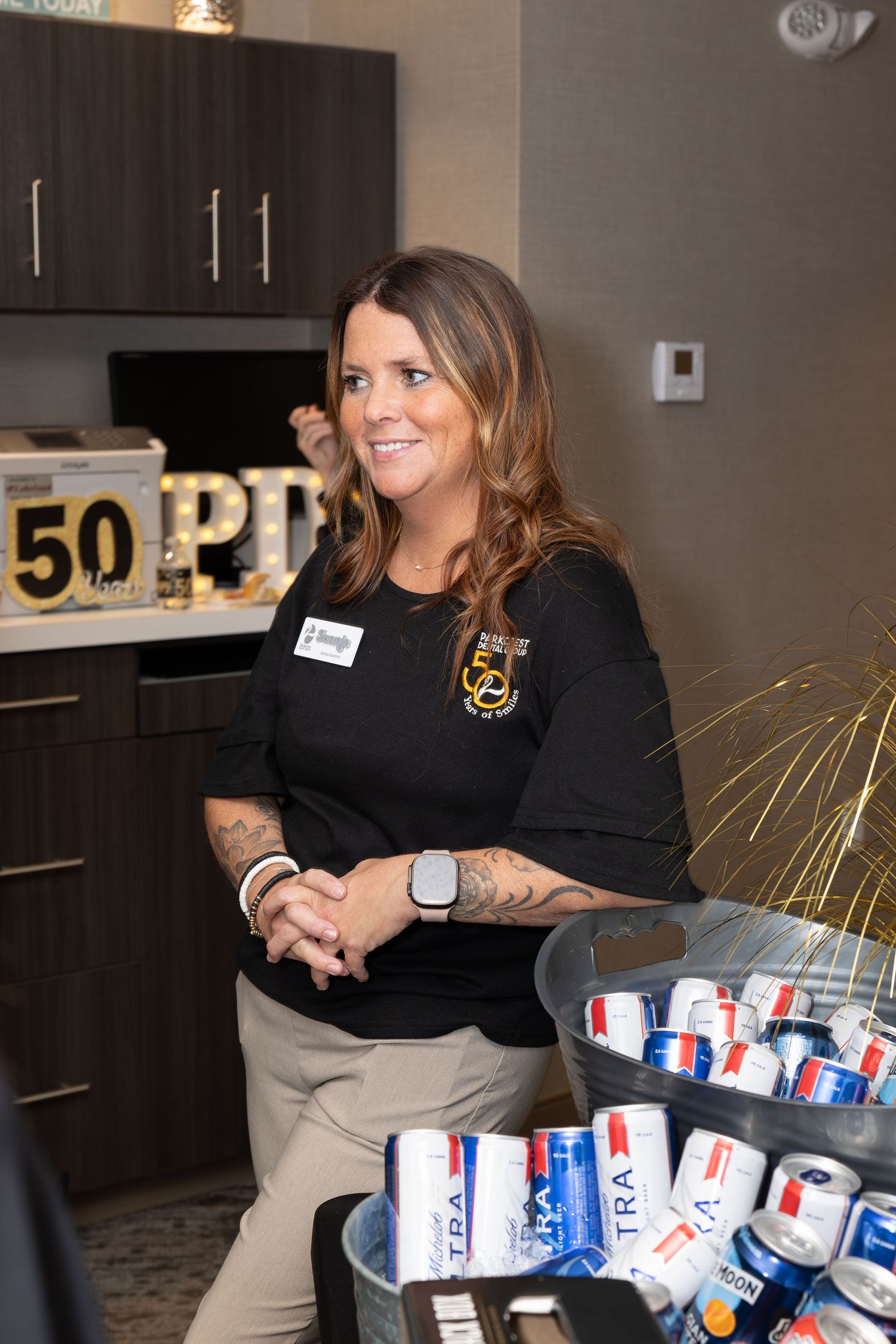 Staff member in black uniform standing next to a table with beverages at an office event.