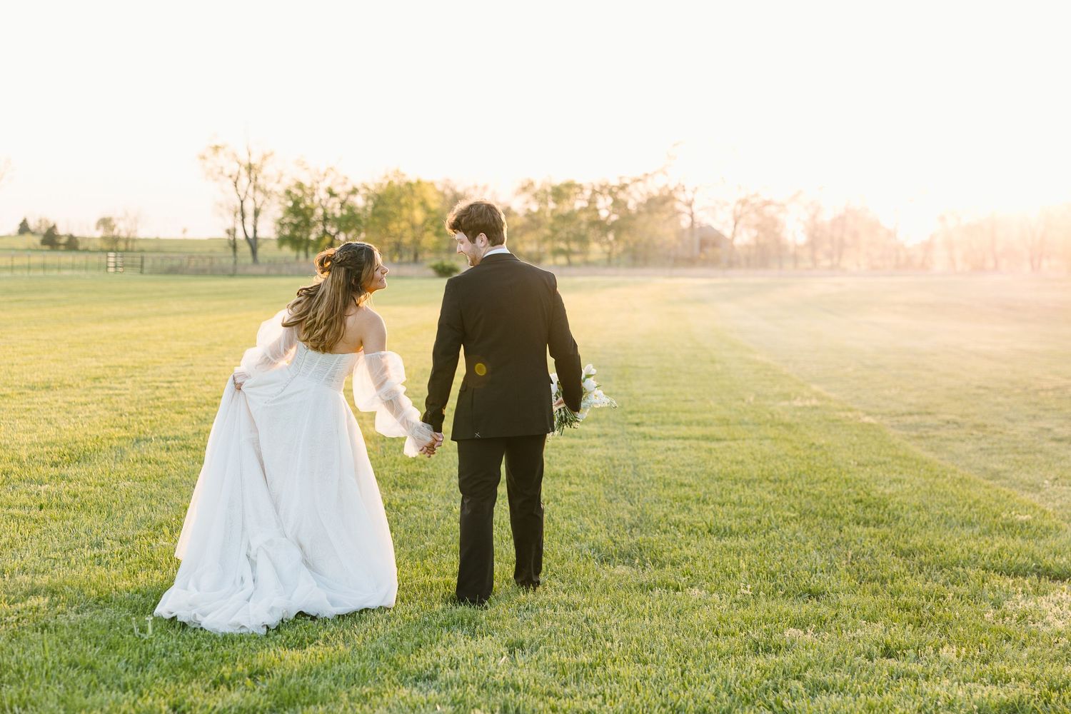 Couple sits together on grassy hill during golden sunset hour in romantic outdoor setting.