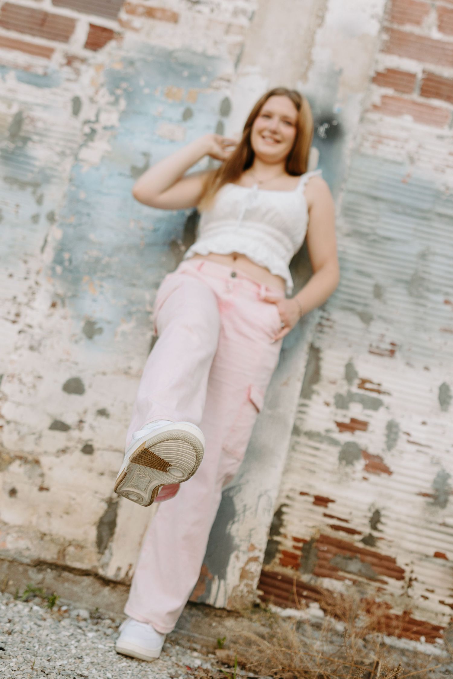 A playful fashion series against a distressed brick wall background showcases light pink pants and white top.