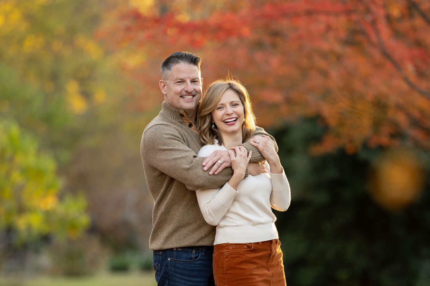 Couple embraces outdoors surrounded by vibrant autumn foliage in a romantic fall photoshoot.