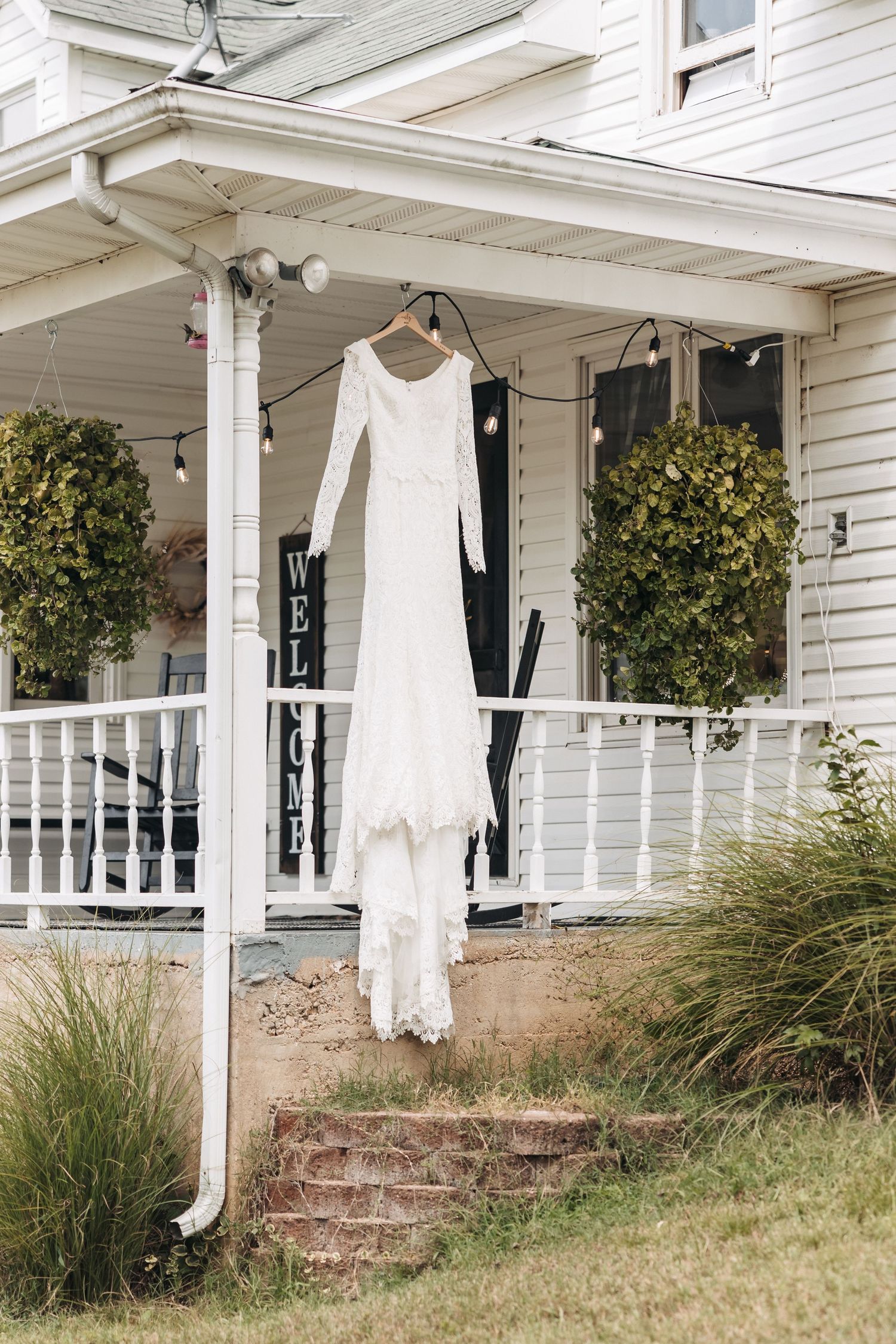 White lace wedding dress hanging on front porch with green topiaries.