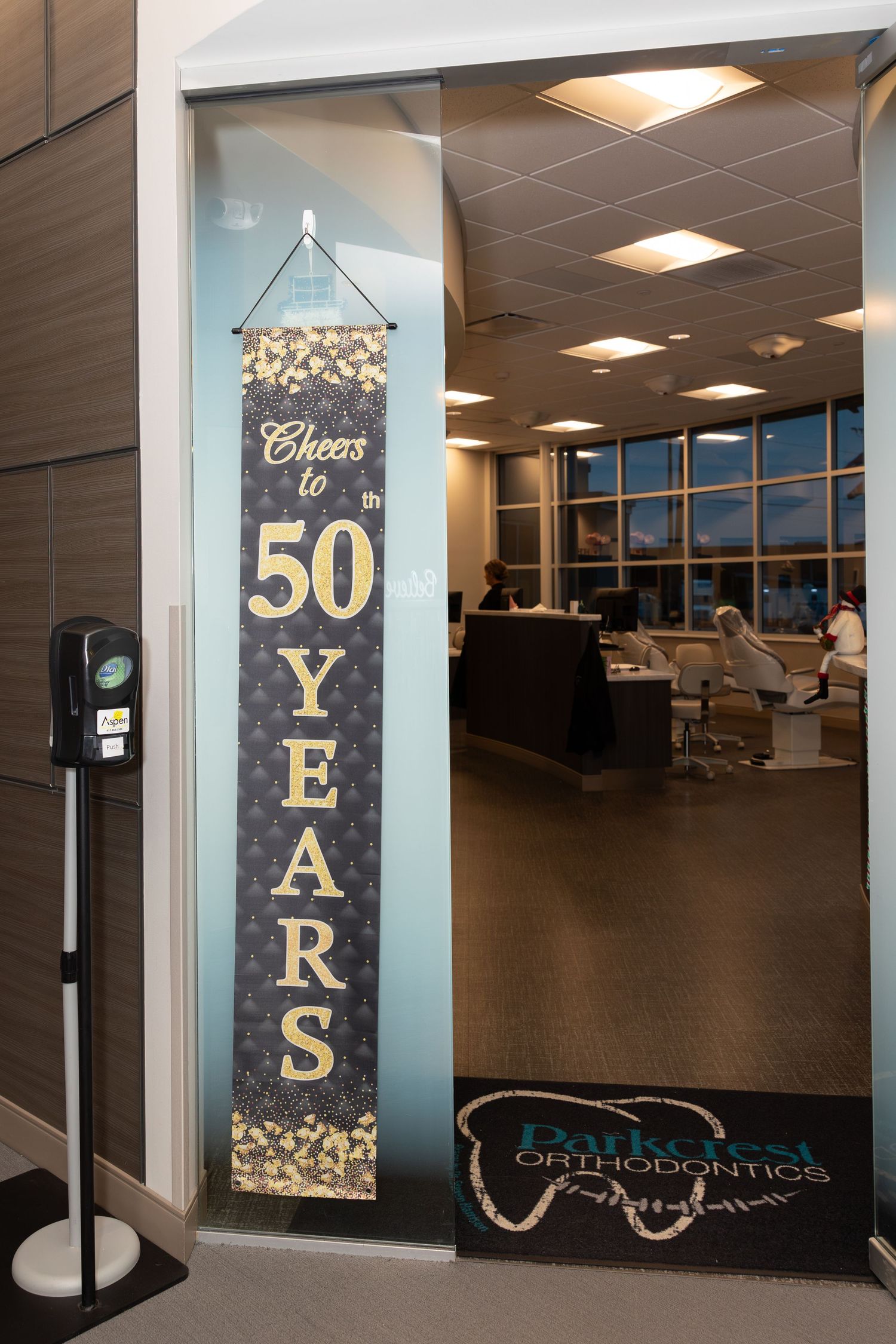 A black and gold banner reading 'Cheers to 50 Years' hangs in a modern office hallway.