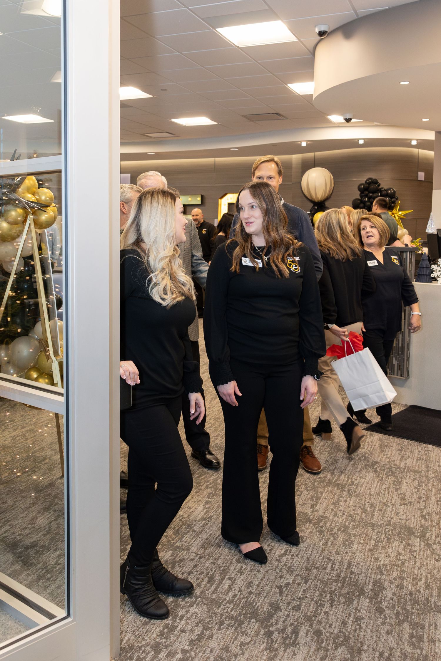 Office celebration with employees in black attire mingling by decorated space.