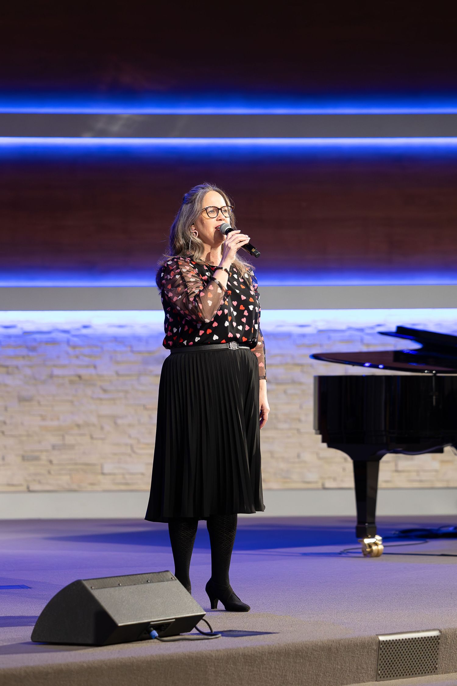 A vocalist performing on stage with a piano and professional lighting.