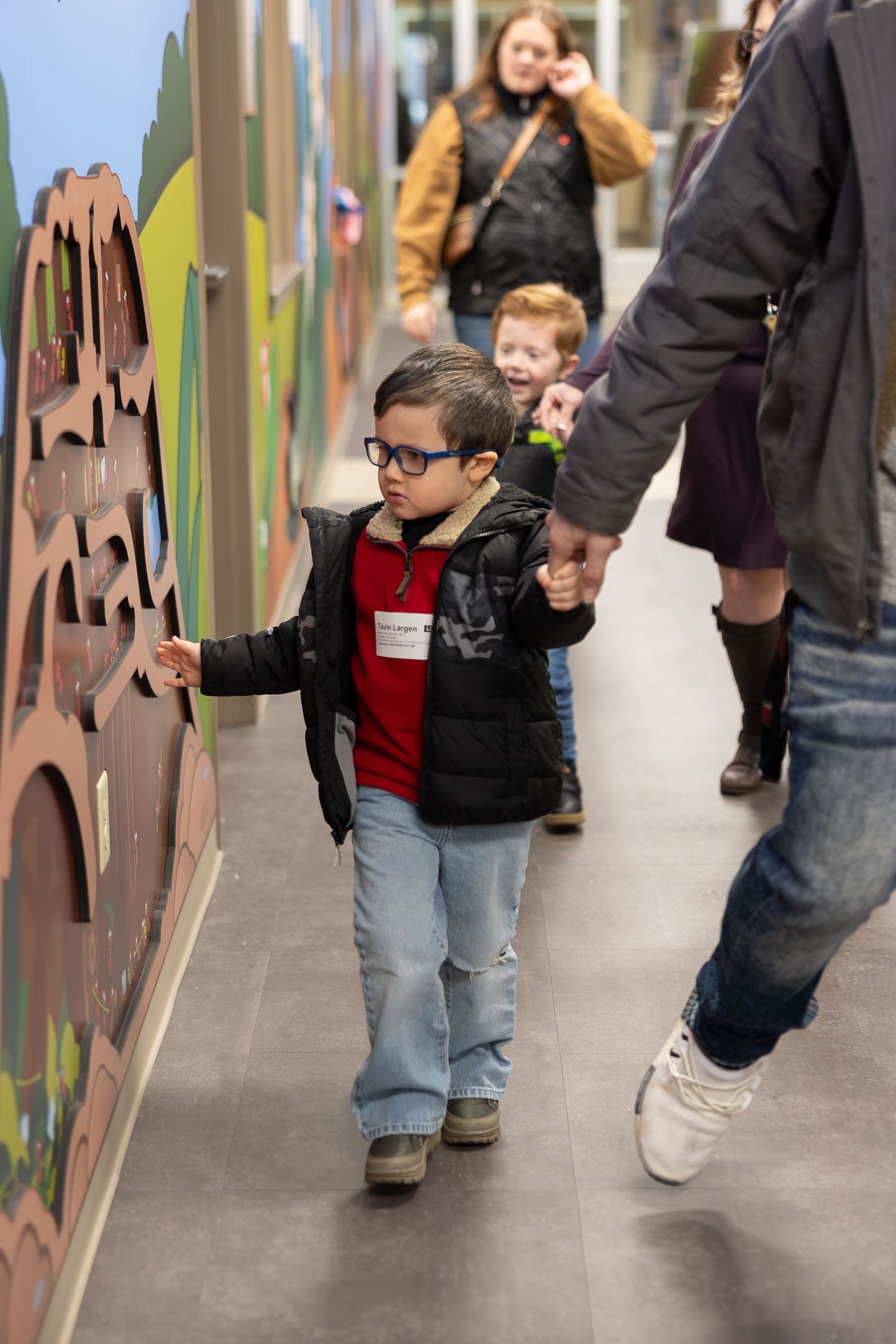 A child explores tactile wall decorations in a brightly decorated corridor.