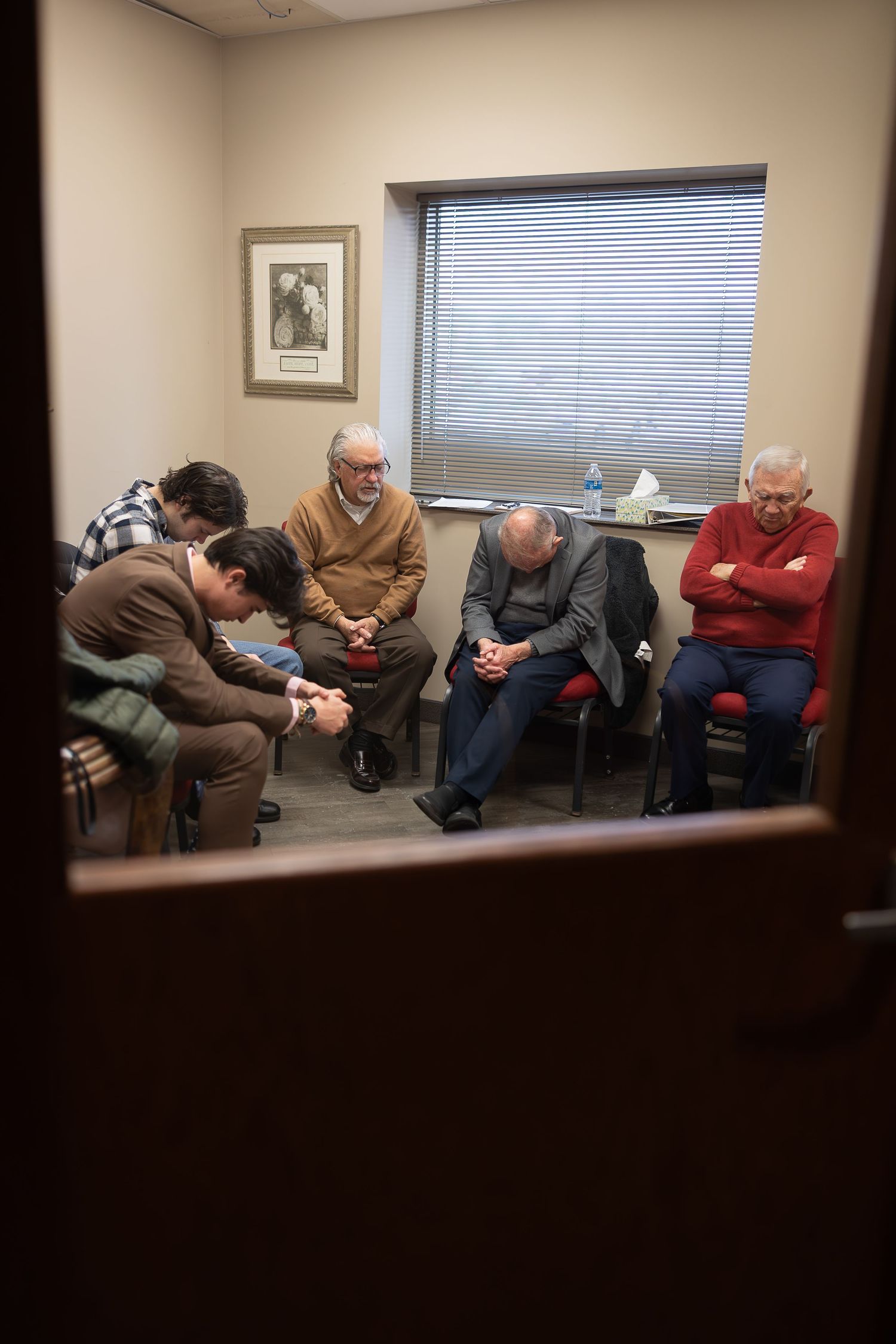 A group meets in a small waiting room with chairs arranged in a circle near a window.