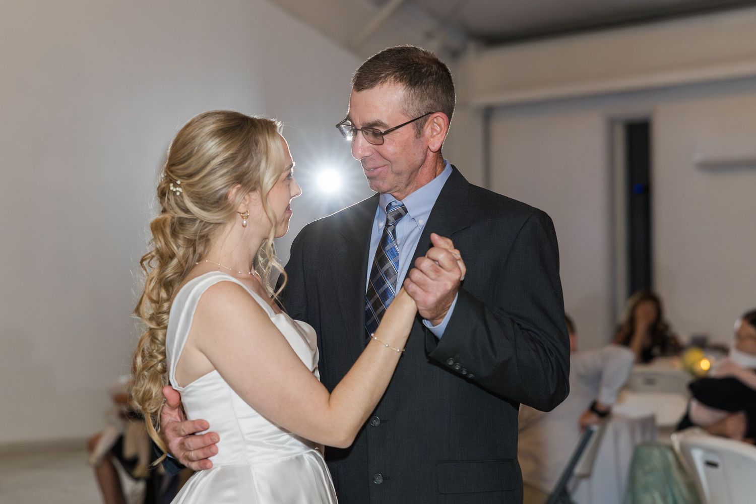 Bride and father sharing an emotional first dance at wedding reception in white dress and dark suit.