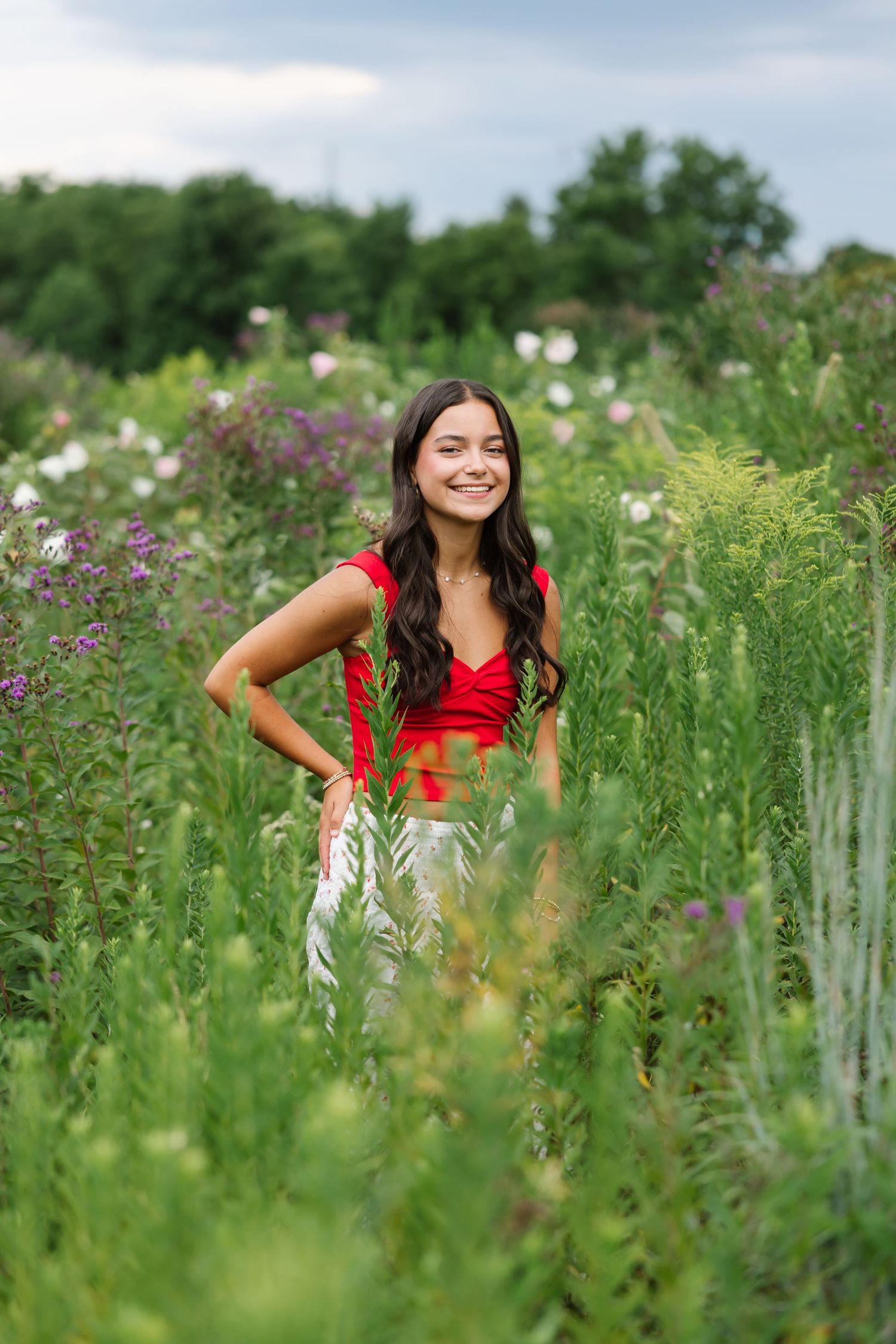 A woman in a red top stands in a lush wildflower meadow on a sunny summer day.