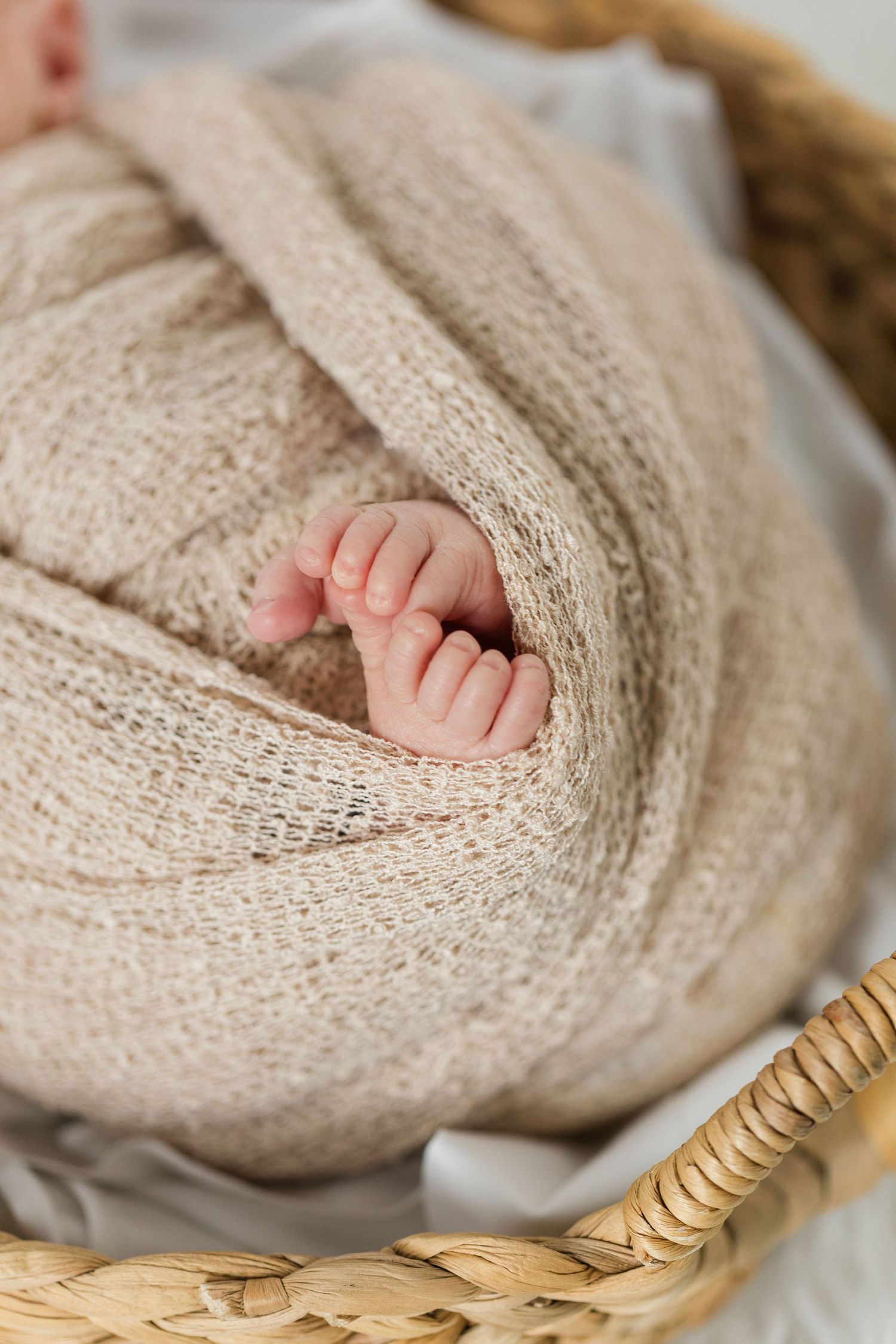 Tiny baby toes peek out from a cozy knitted beige blanket in a woven basket.
