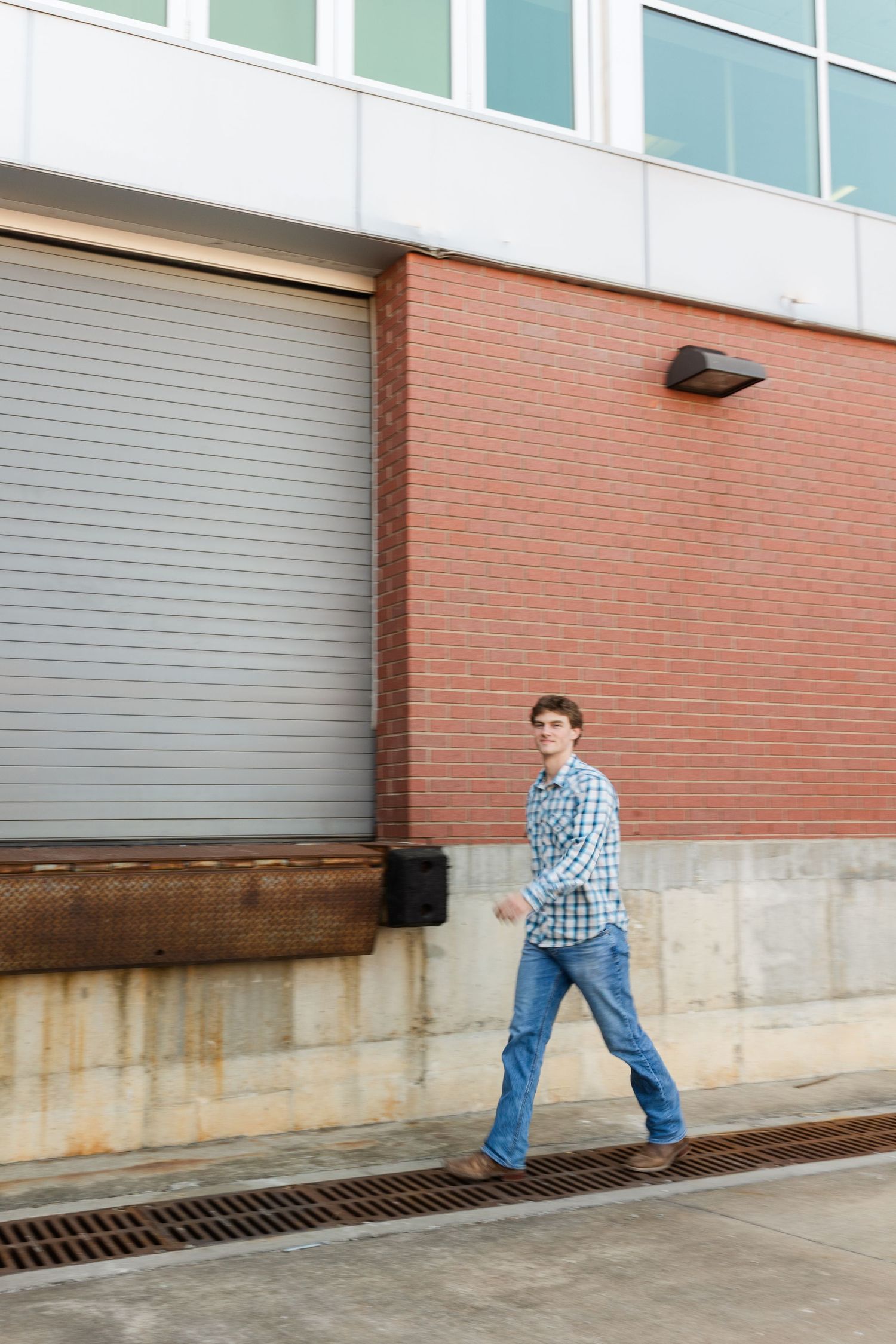 A person in blue plaid walks past a brick building with a metal loading door.