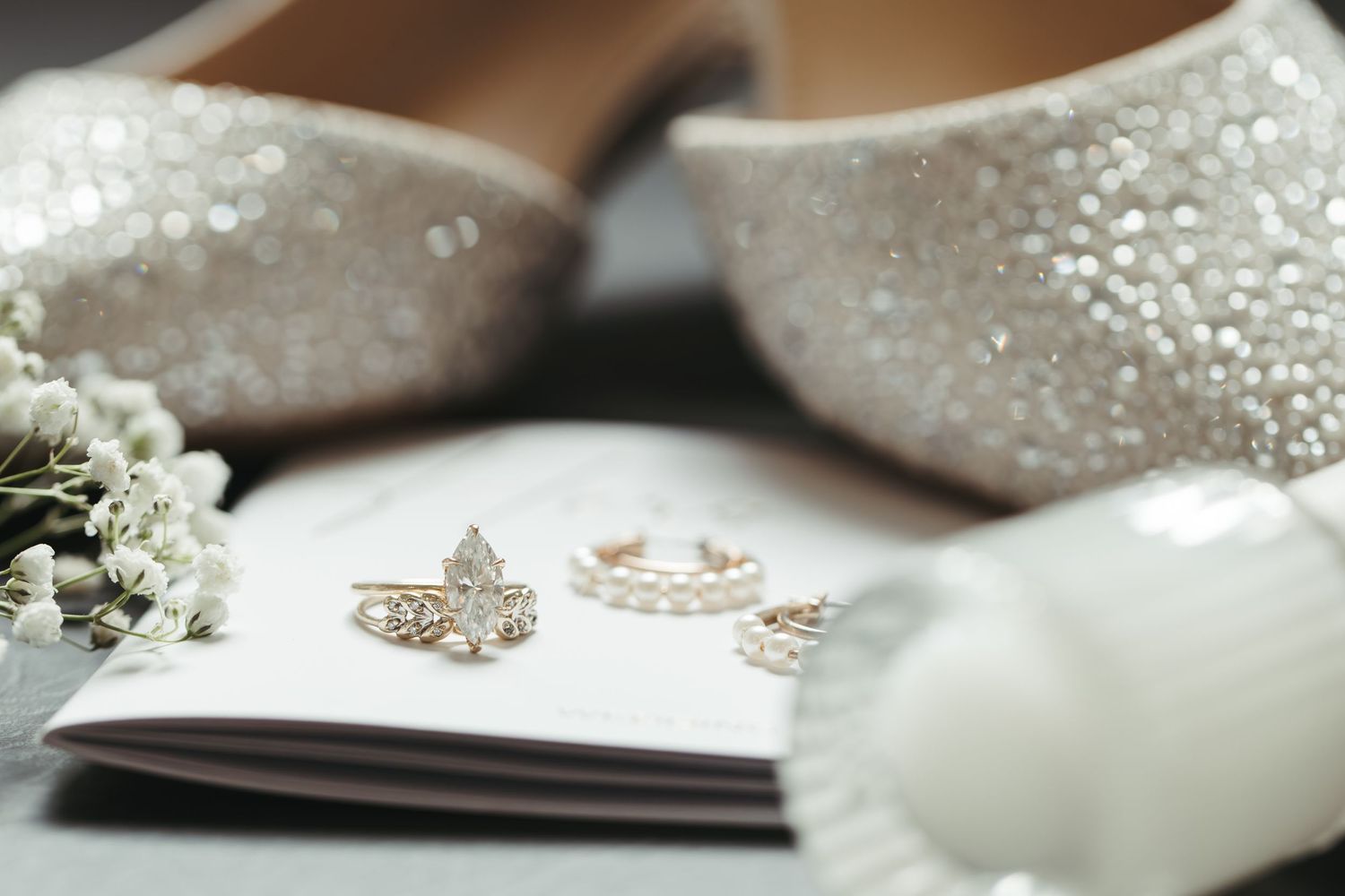 Glittering bridal shoes with engagement ring and delicate white flowers.