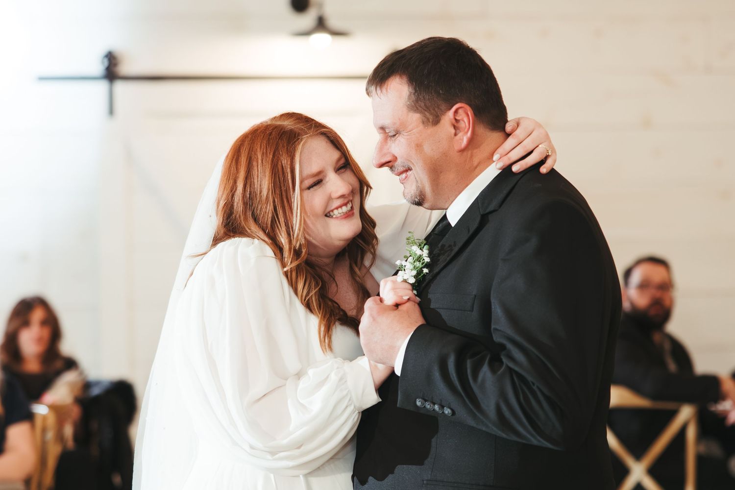 A couple shares an intimate first dance moment at their wedding reception with guests seated in the background.
