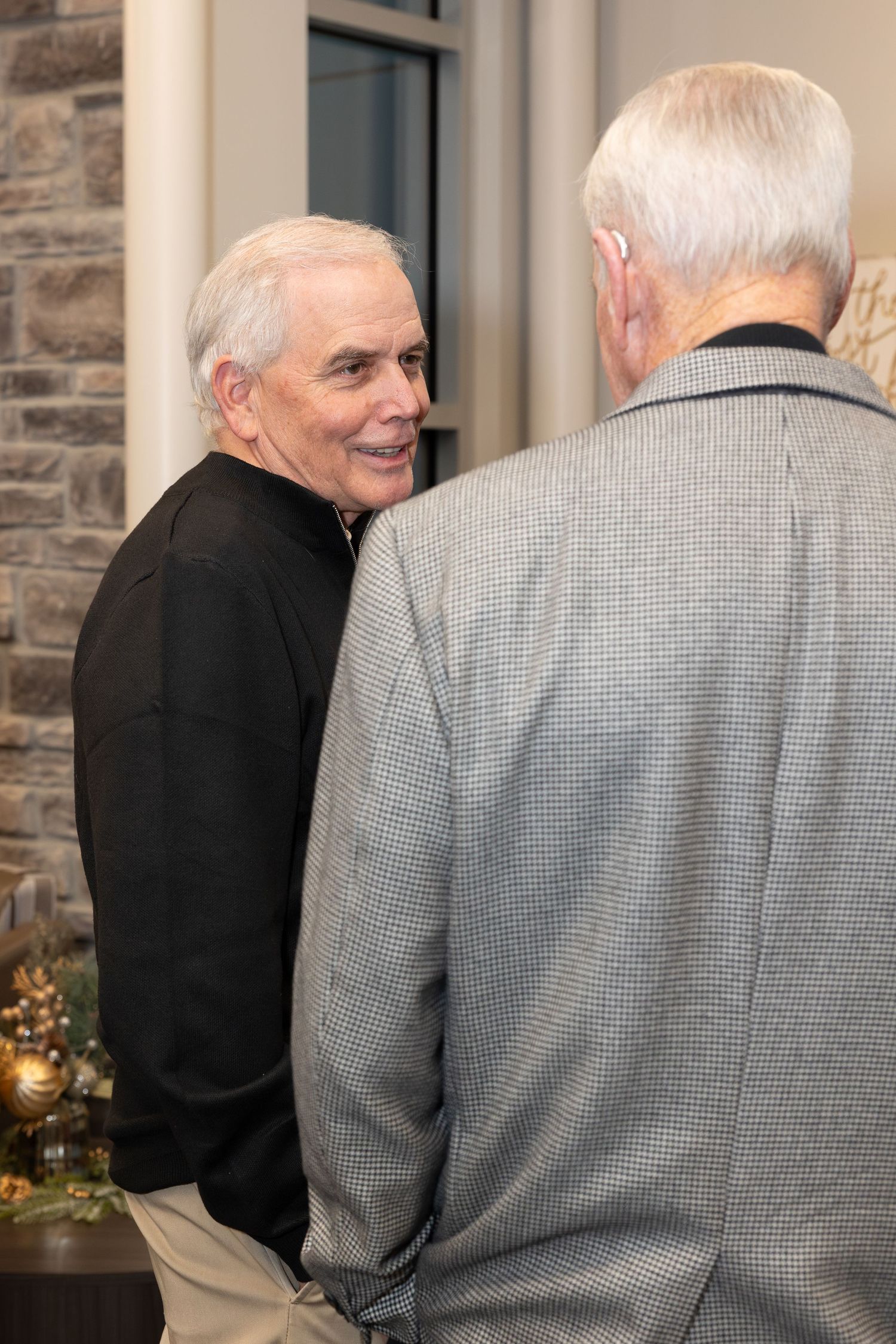 Two people engaged in conversation near a stone wall with holiday decorations.