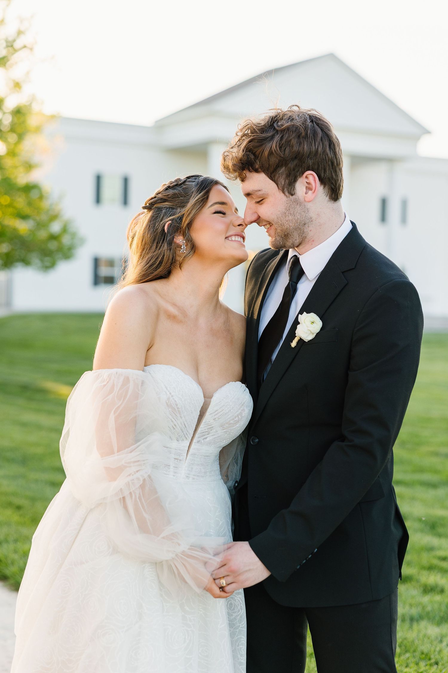 A bride and groom share an intimate moment on their wedding day in an outdoor garden setting at sunset.