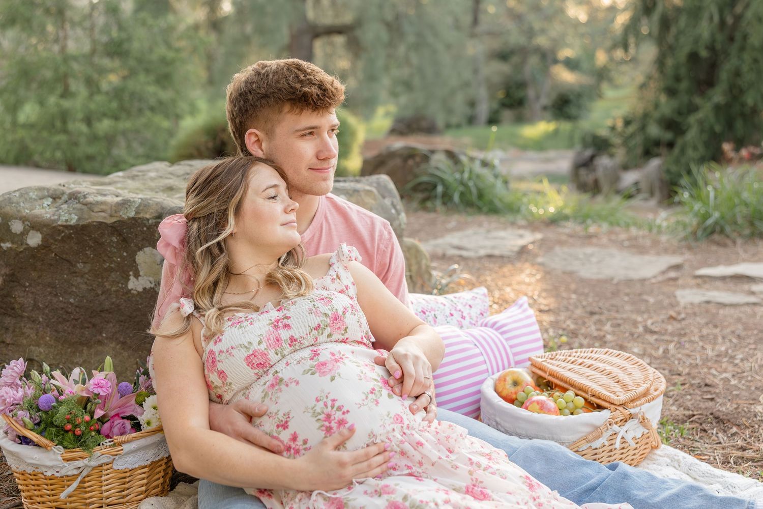 A couple enjoys a romantic picnic outdoors with a basket of food and flowers on a warm sunny day.