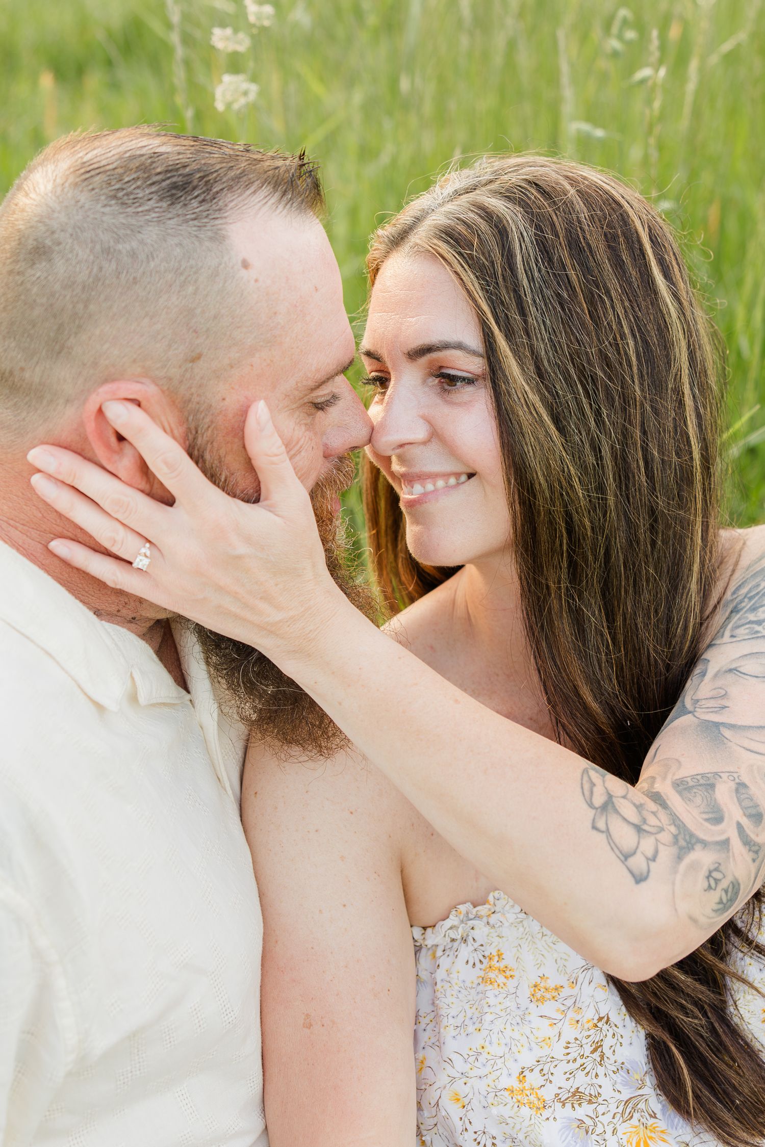 Romantic couple sharing an intimate moment in a grassy meadow as she tenderly touches his face.