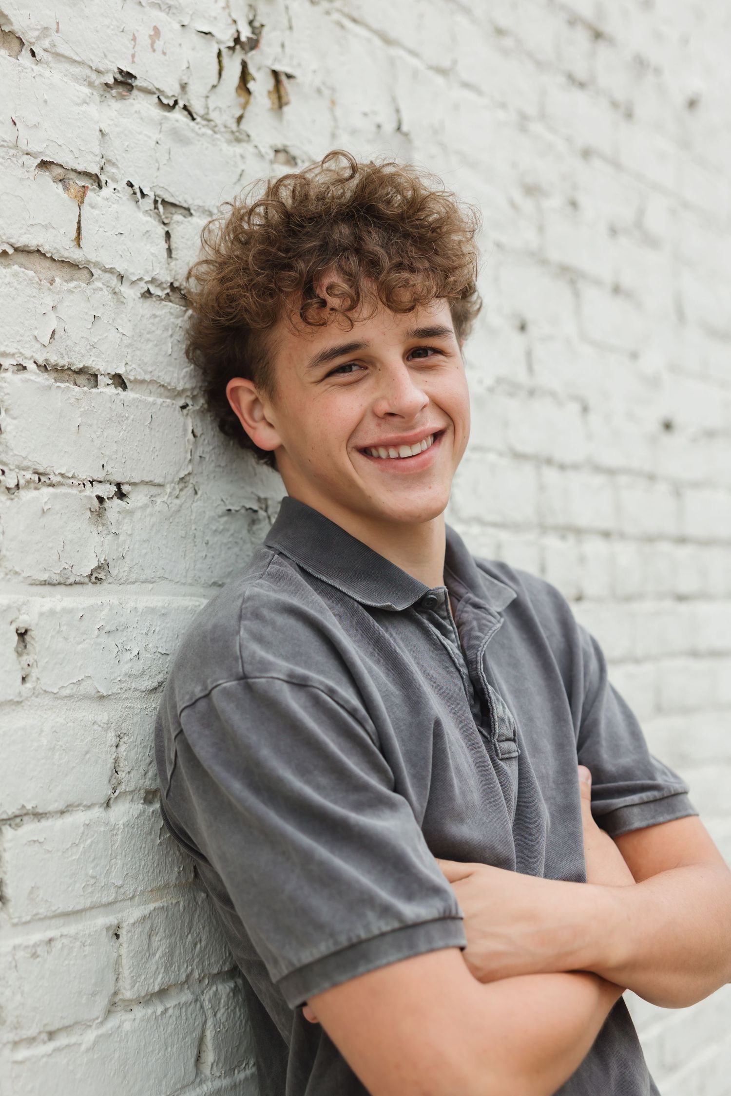 Three similar photos show a casual posed portrait against a white brick wall.