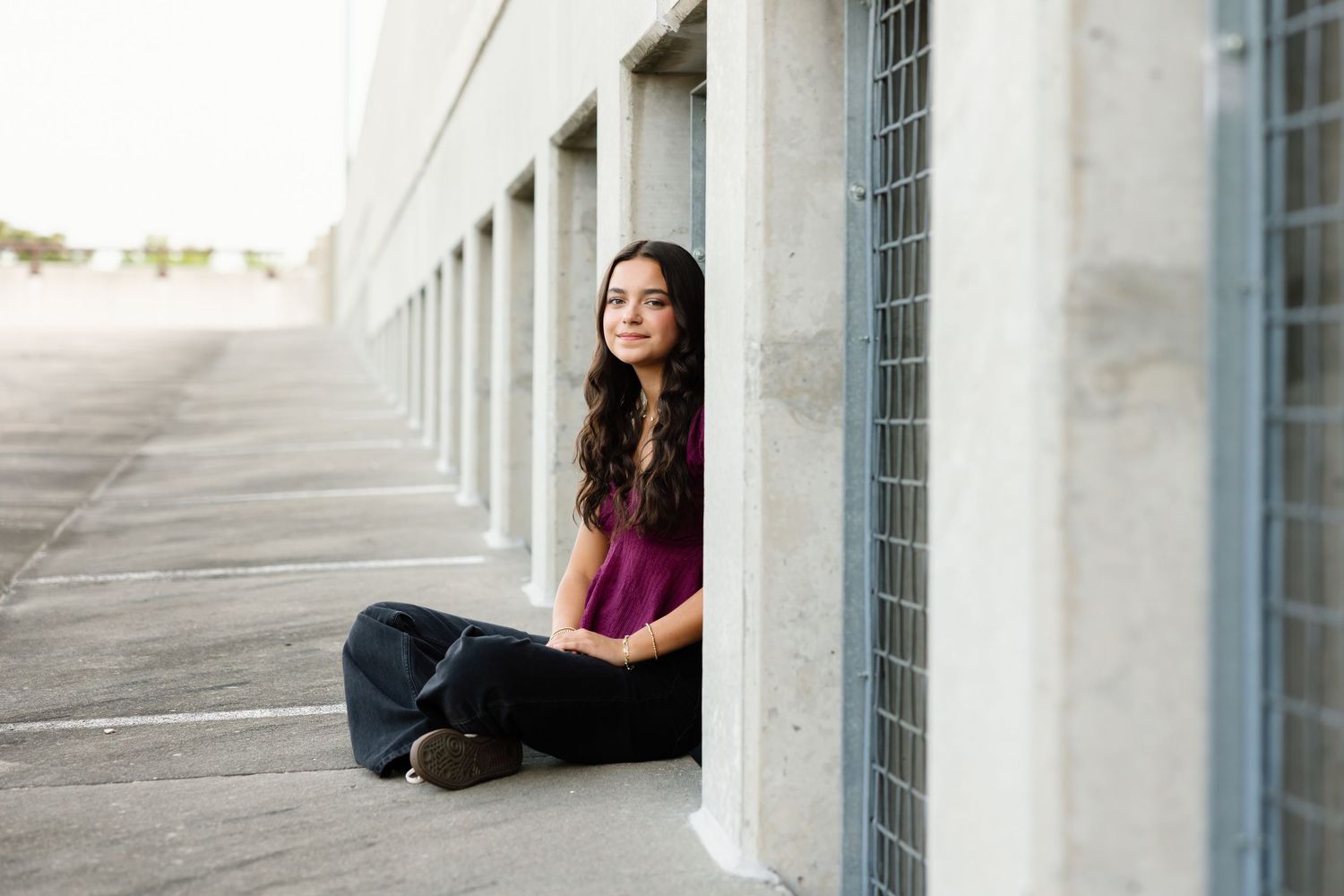 A casual portrait against white concrete columns in burgundy top and dark pants.