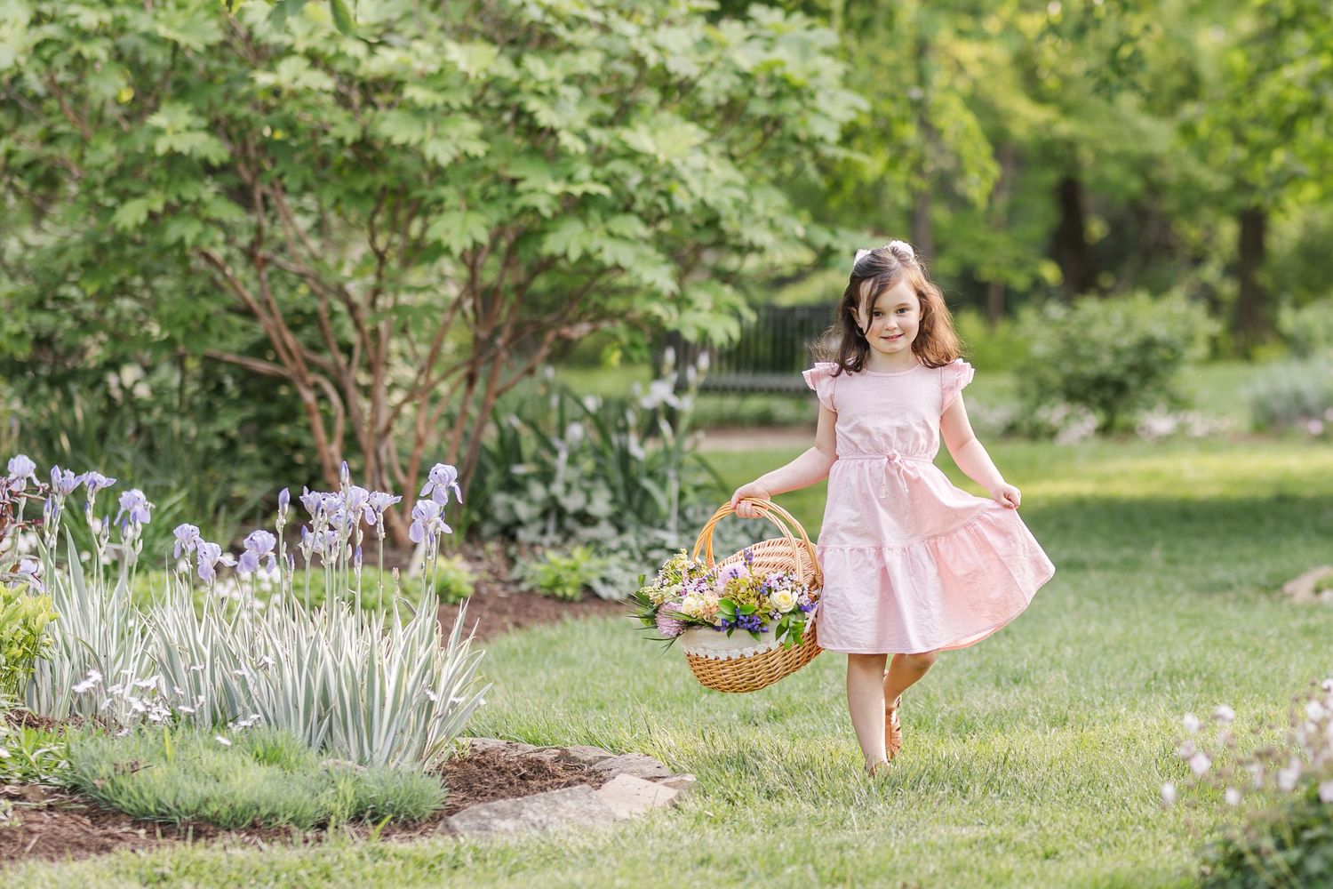 A figure in a pink dress skips through a lush garden pathway filled with flowering lavender plants and greenery on a sunny day.