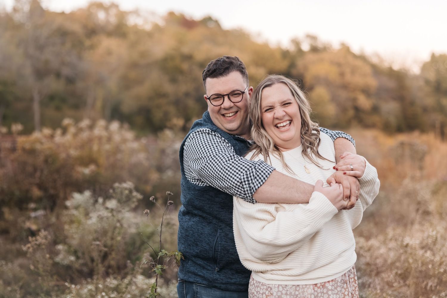 A couple embraces while laughing together in an outdoor fall setting at sunset.