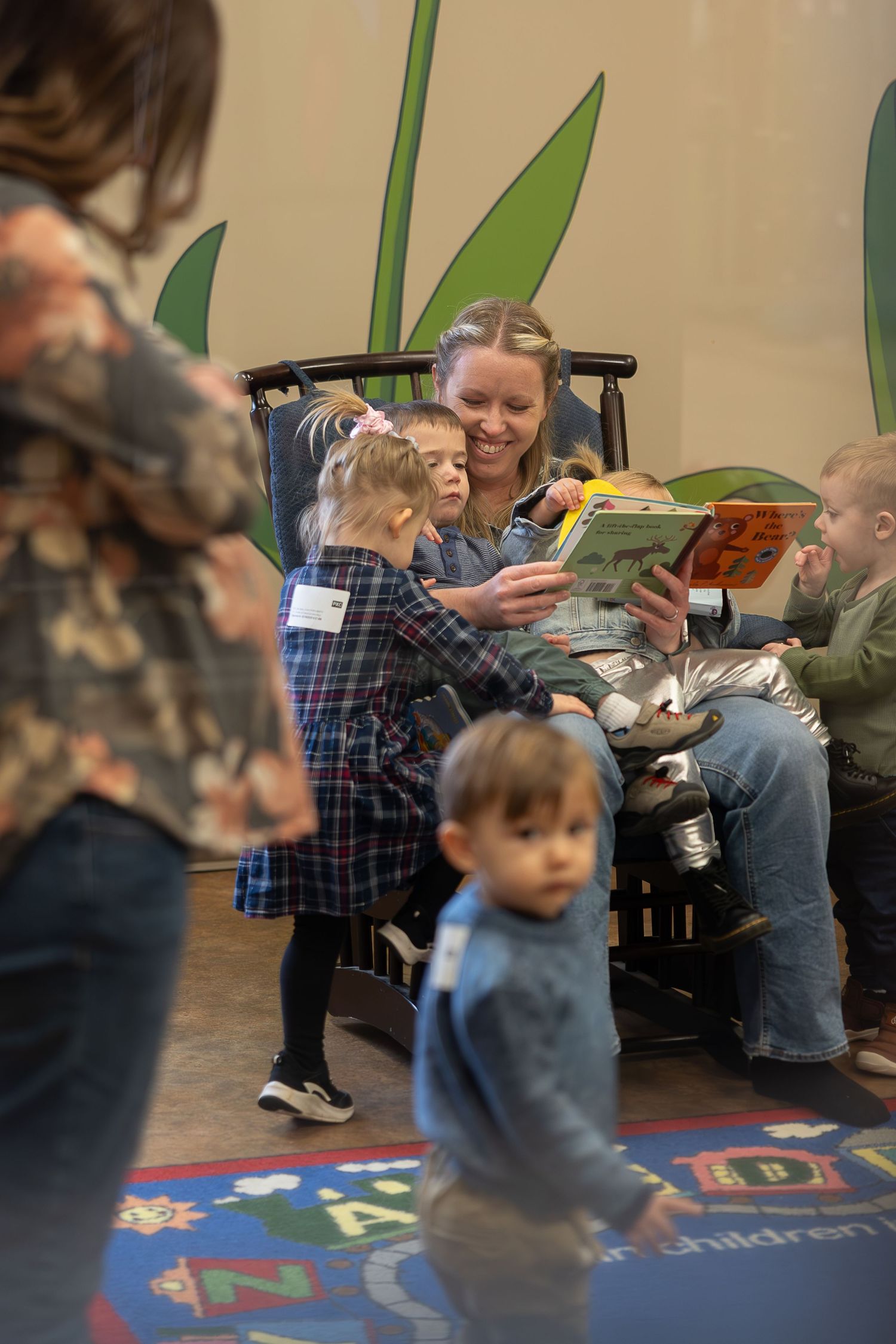 Children gathered around for story time on alphabet rug in classroom setting.