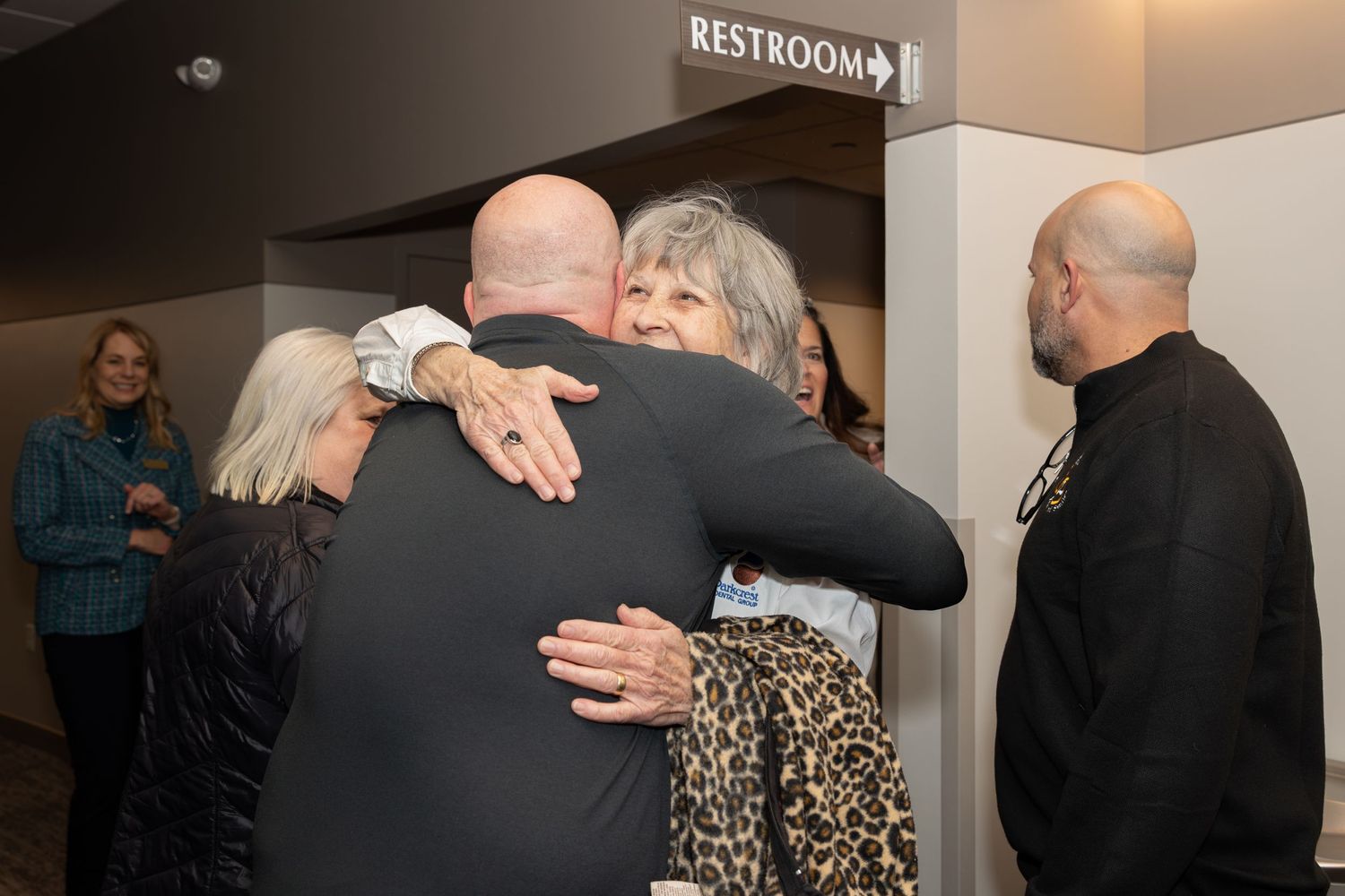 A group of people sharing a warm embrace near a restroom sign.